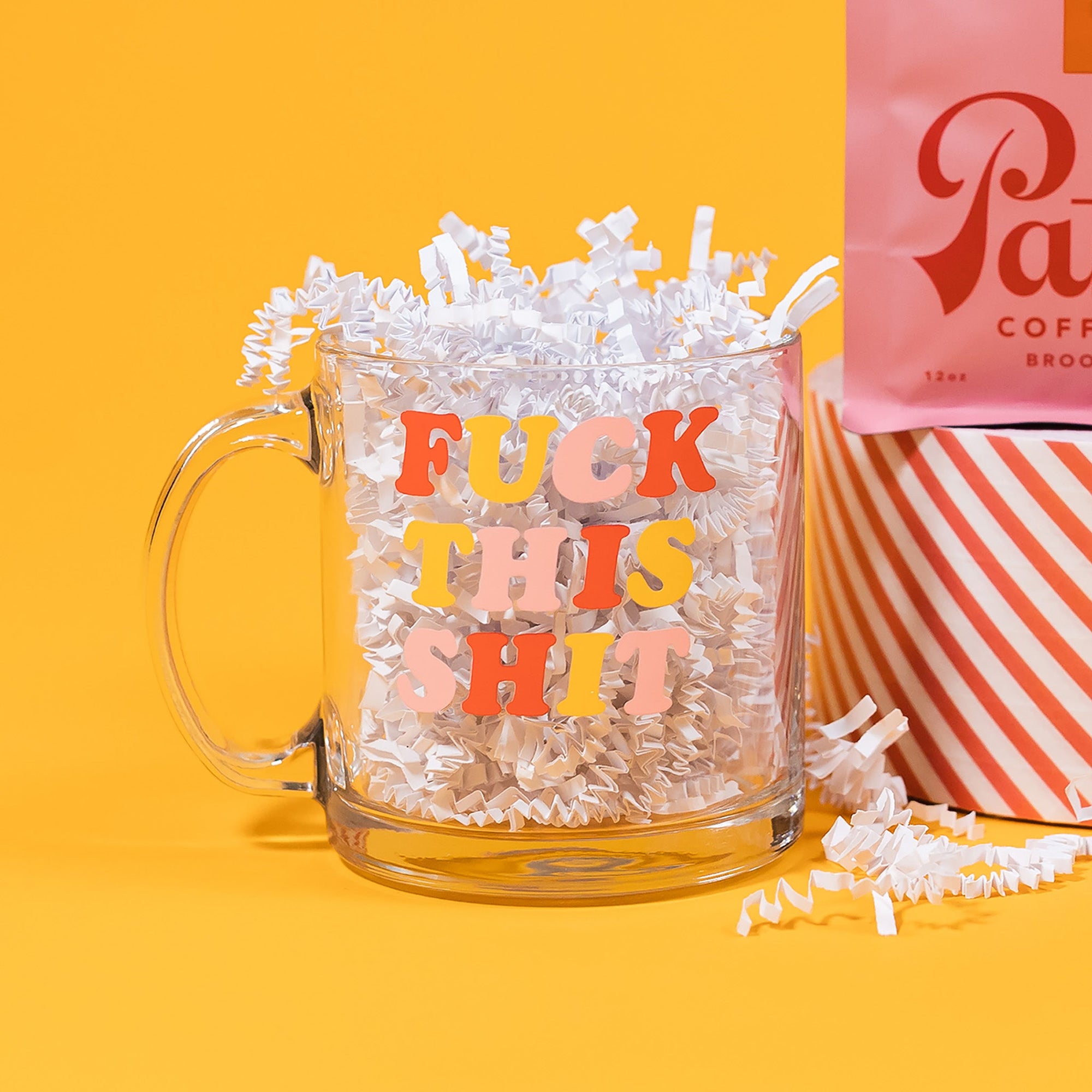 On a sunny mustard background sits a mug with white crinkle in it. This clear mug says "FUCK THIS SHIT" in a colorful, thick serif font. The colors are watermelon pink, sunny mustard and light pink.