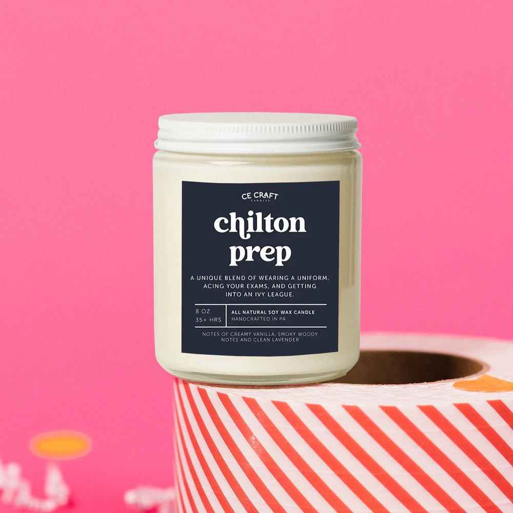 On a hot pink background sits a candle on a red and white packing tape with colorful confetti and white crinkle scattered around. It is has a navy label with white text. This Chilton Prep Candle has notes of creamy vanilla, smoky woody notes and clean lavender & is the perfect scent for your die hard Gilmore Girls Fan! This standard sized 8 oz jar has a burn time of approximately 35+ hours, perfect for bathrooms, dressers, countertops, and nightstands; or in front of your Netflix reruns of Gilmore!
