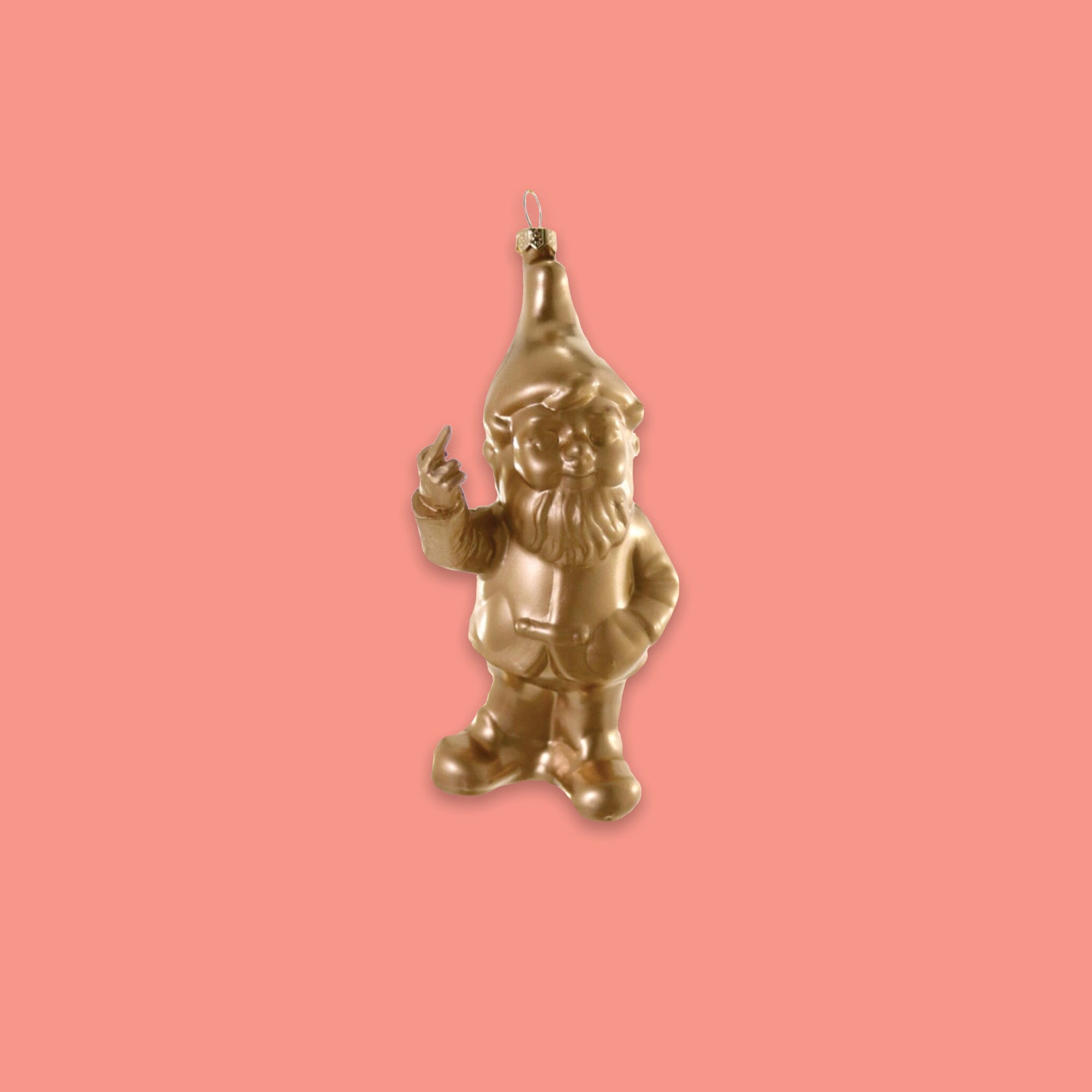 On a coral pink background sits an ornament. This is a gold glass ornament of a gnome giving the middle finger.