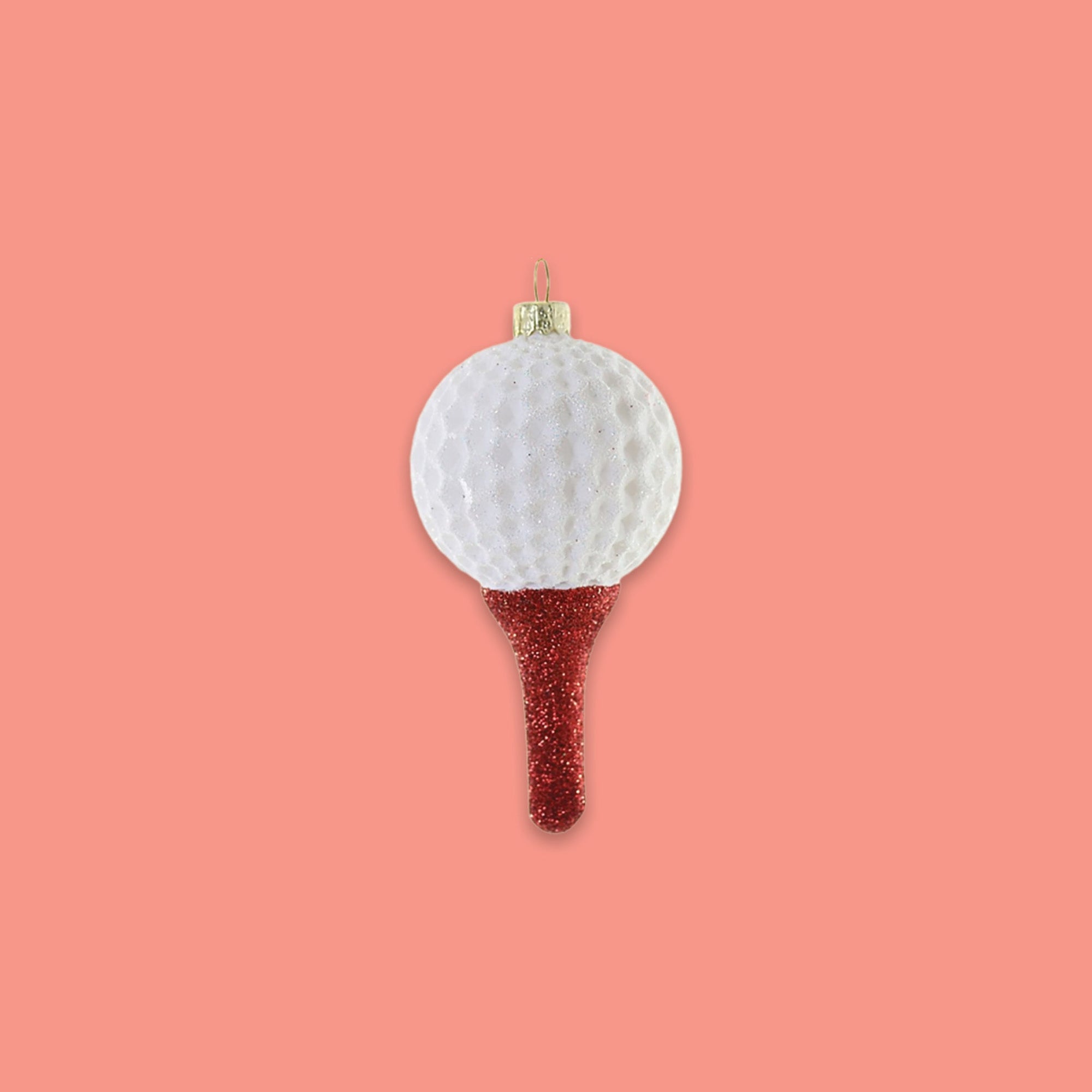 On a coral pink background sits an ornament. This is a white glitter golf ball sitting on top of a red glitter tee.