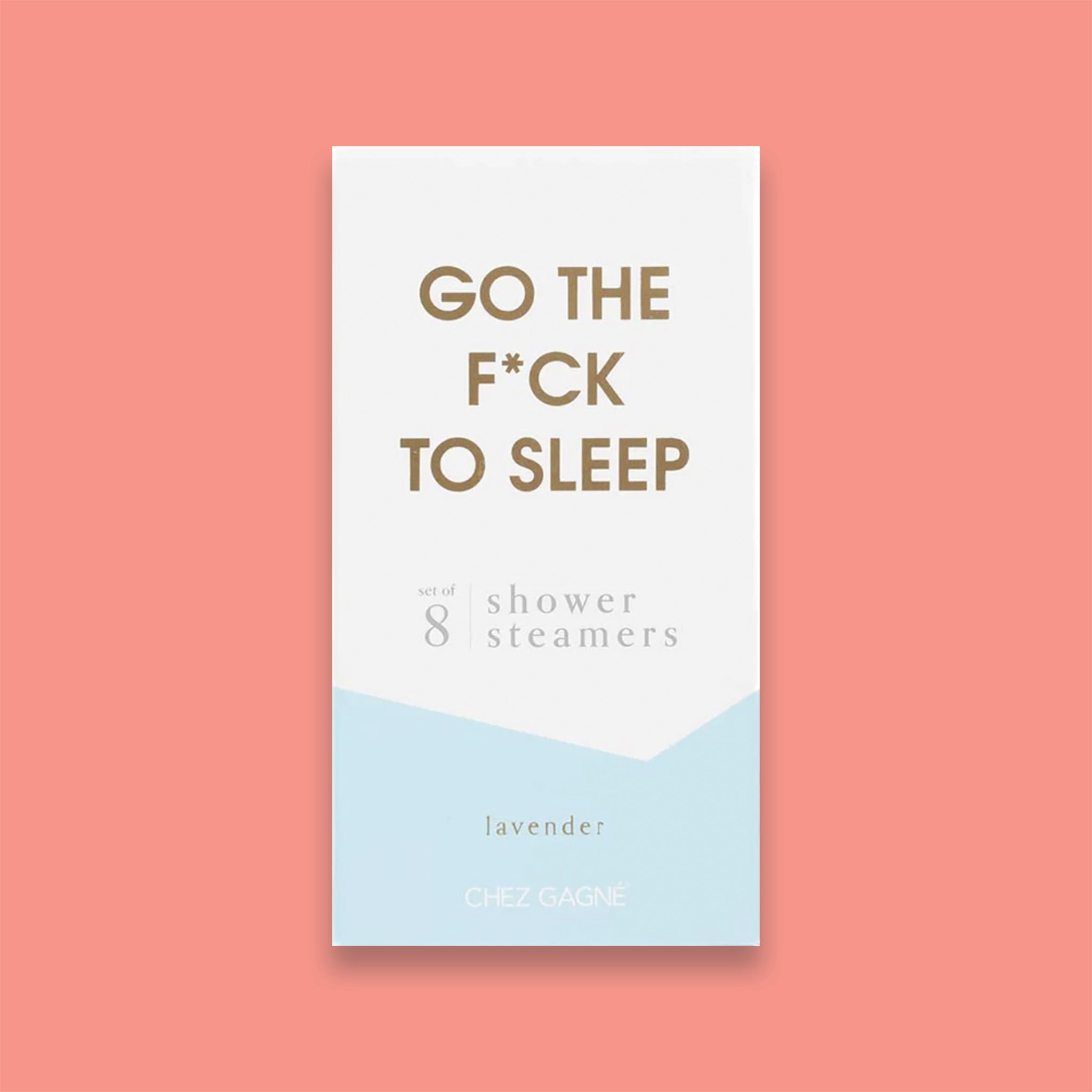 On a light coral background sits a box. This picture is a close-up of a white and light blue package that says "GO THE F*CK TO SLEEP" in gold foil, all caps block lettering. Under it says "set of 8" and " shower steamers" in grey, lowercase serif font. At the bottom it says "lavender" in gold foil, lower case serif font.