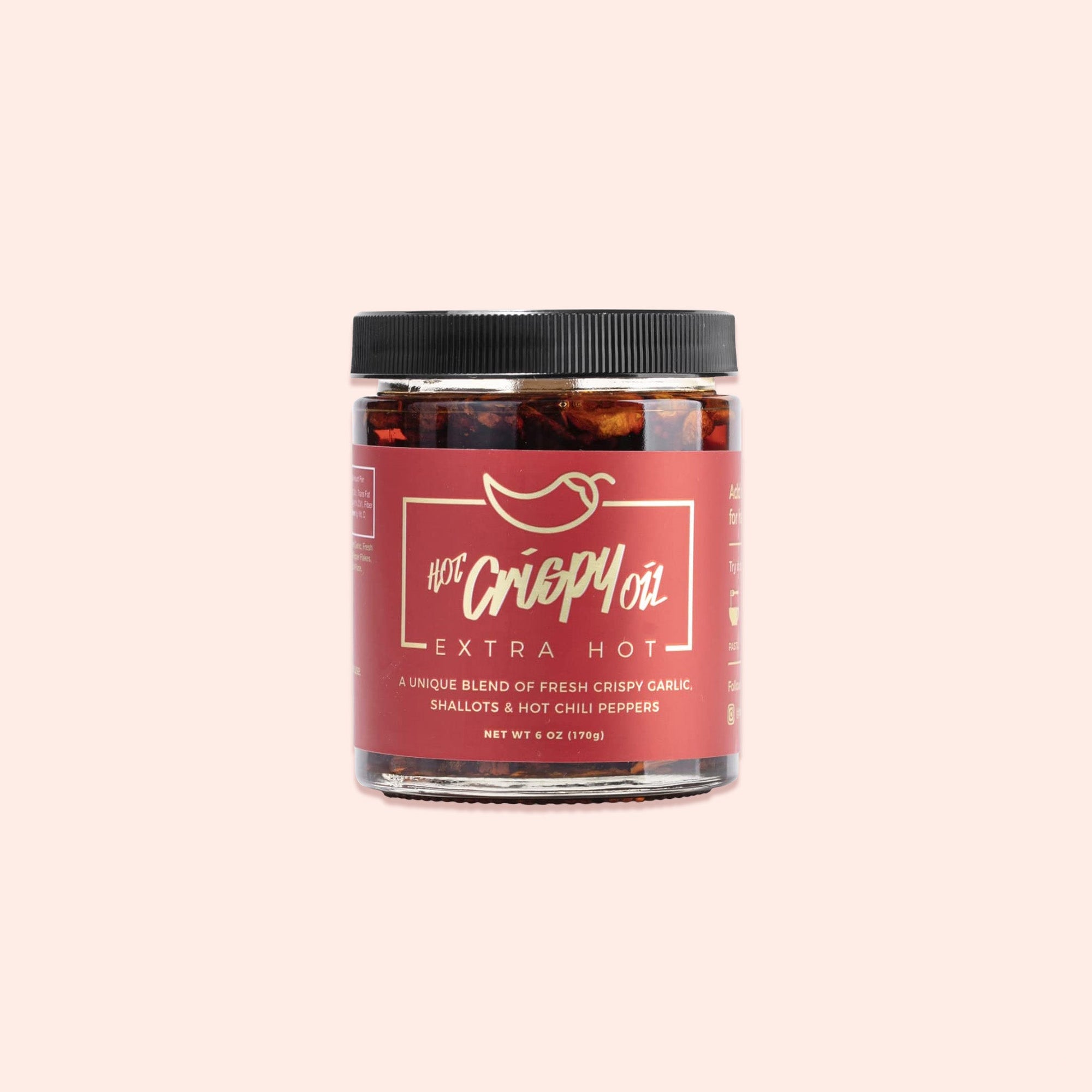 On a light pink background sits a jar with a black lid and black label. It has a gold outlined box and a chili pepper above it. It says in gold "HOT Crispy Oil EXTRA HOT." It also says in red "A UNIQUE BLEND OF FRESH CRISPY GARLIC, SHALLOTS & HOT CHILI PEPPERS." NET WT 6 OZ (170G)