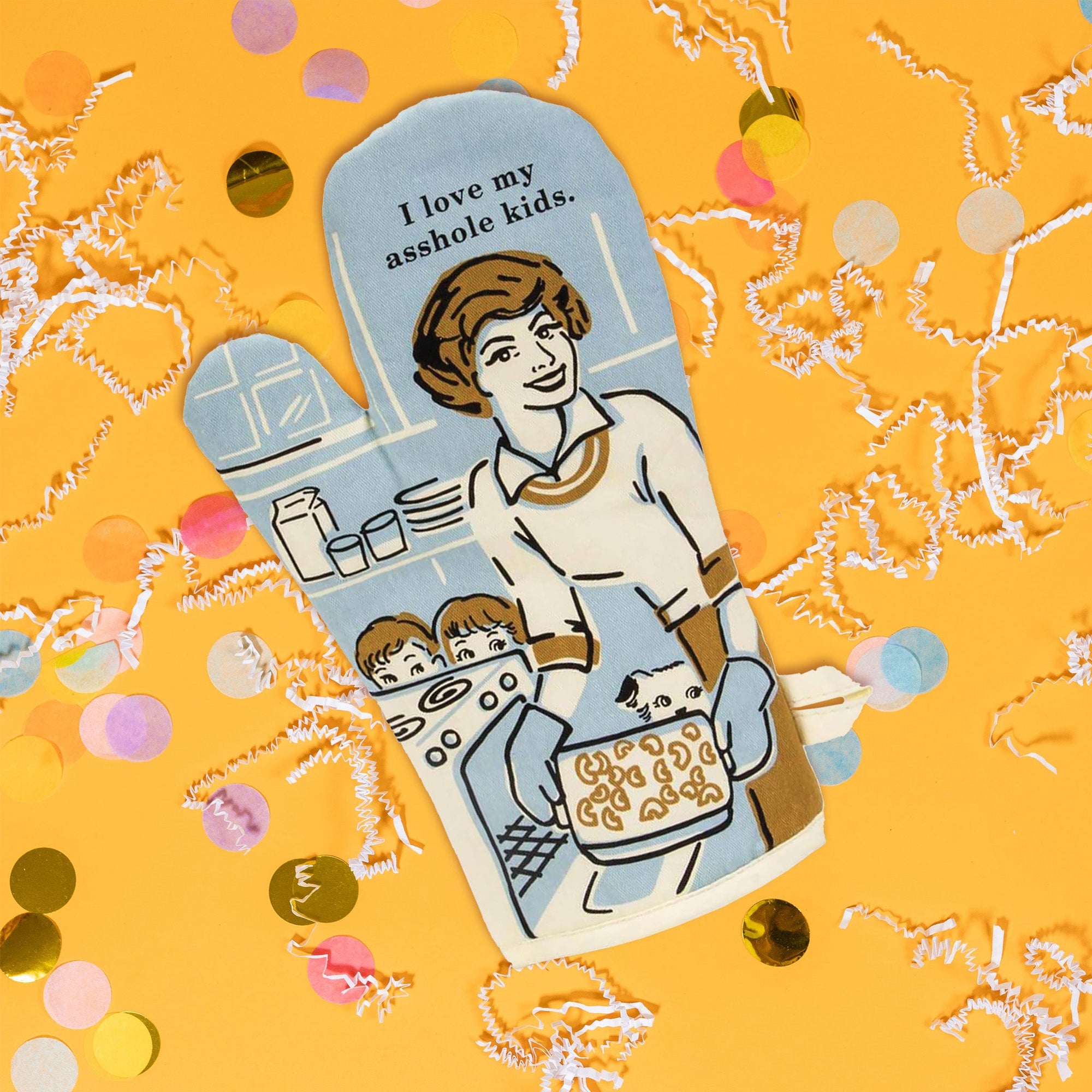 On a sunny mustard background sits an oven mitt with white crinkle and big, colorful confetti scattered around. The front of this light blue oven mitt has a vintage illustration of a woman cooking with a stove, two children and a dog peeking behind her and the stove. The colors are light blue, gold, black, and white. At the top it says "I love my asshole kids." in black serif font.