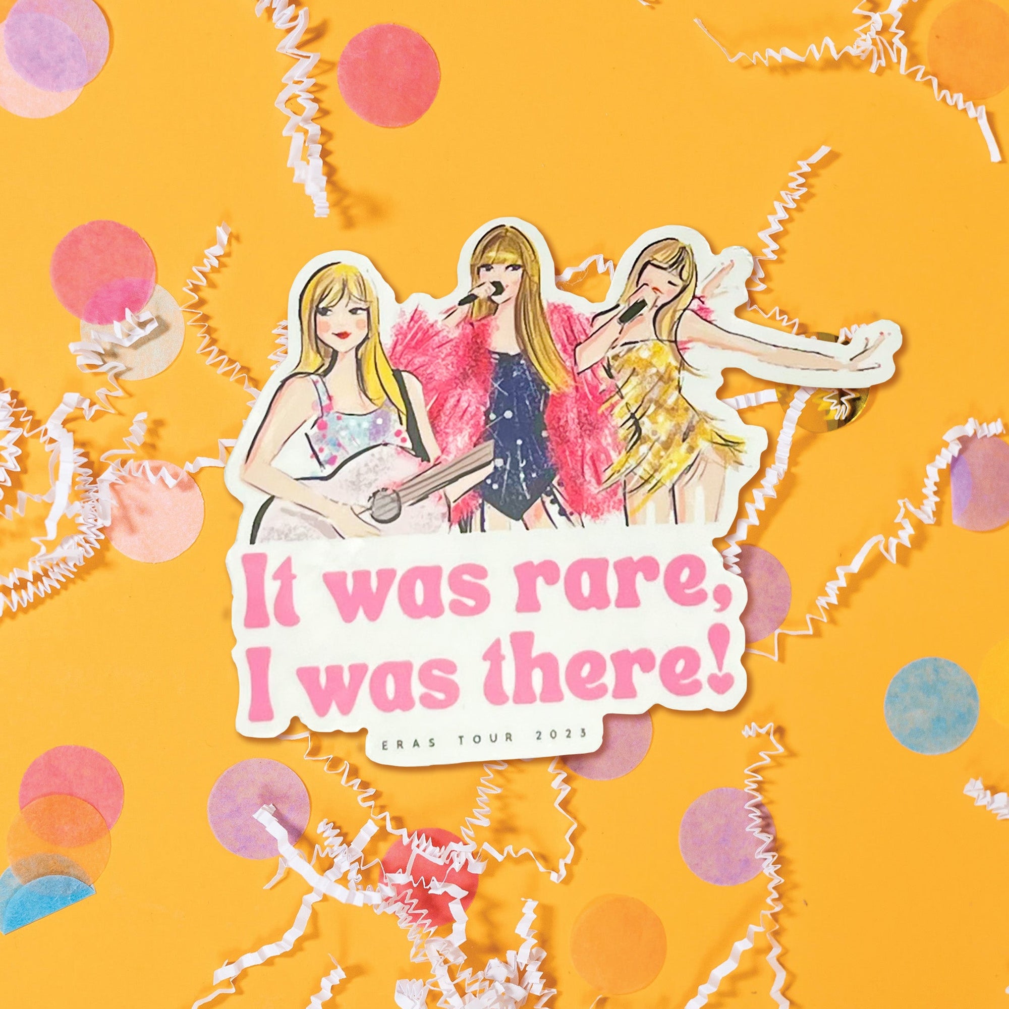 On a sunny mustard background sits a sticker with white crinkle and big, colorful confetti scattered around.Taylor Swift inspired sticker says is an illustration of three different Taylor Swifts dressed in different costumes. It says "It was rare, I was there!" in bubble gum pink, fat font. It also says "ERAS TOUR 2023" in black lettering.