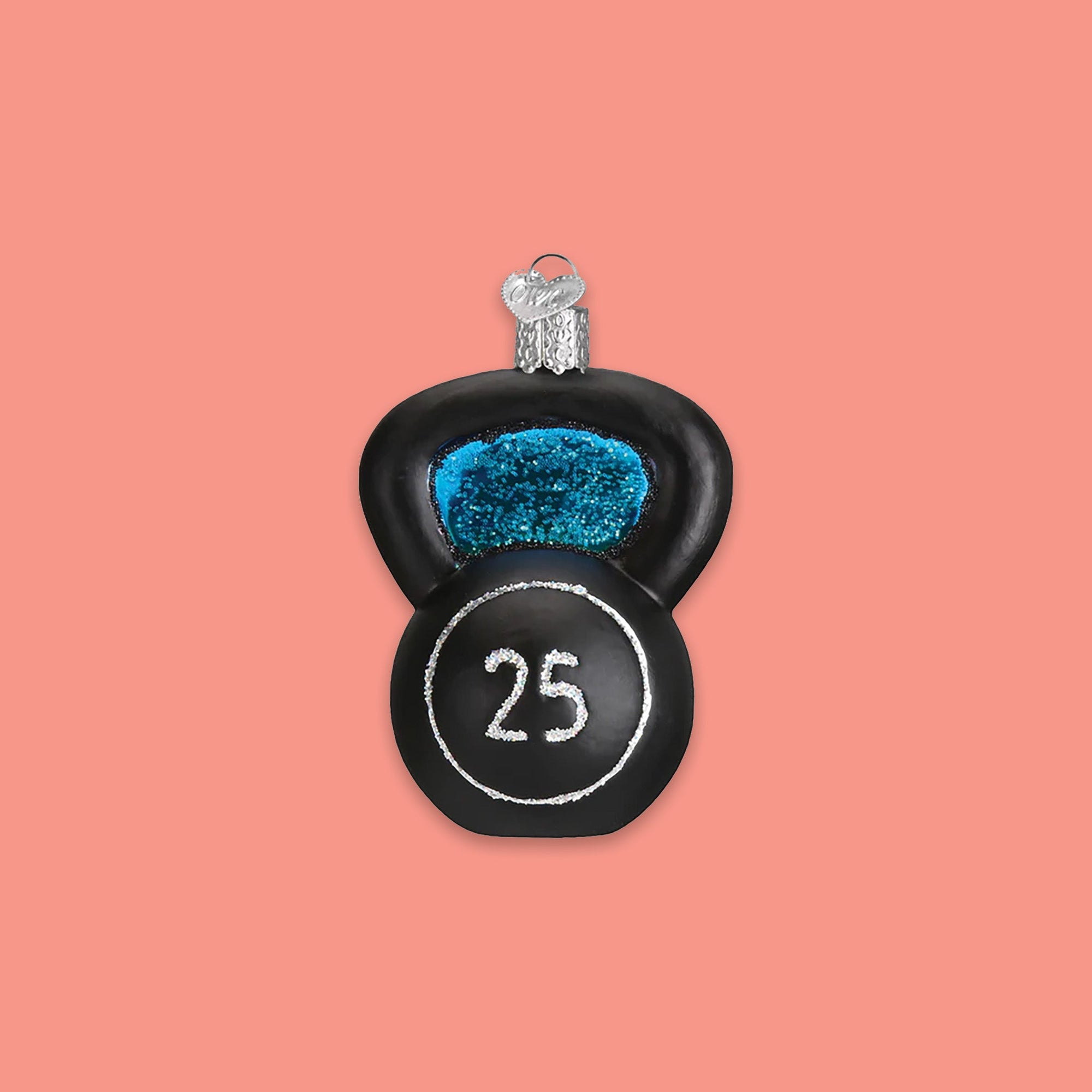 On a coral pink background sits an ornament. This glass ornament is of a black kettlebell with a silver glitter circle and the number '25' in silver glitter inside the circle. 