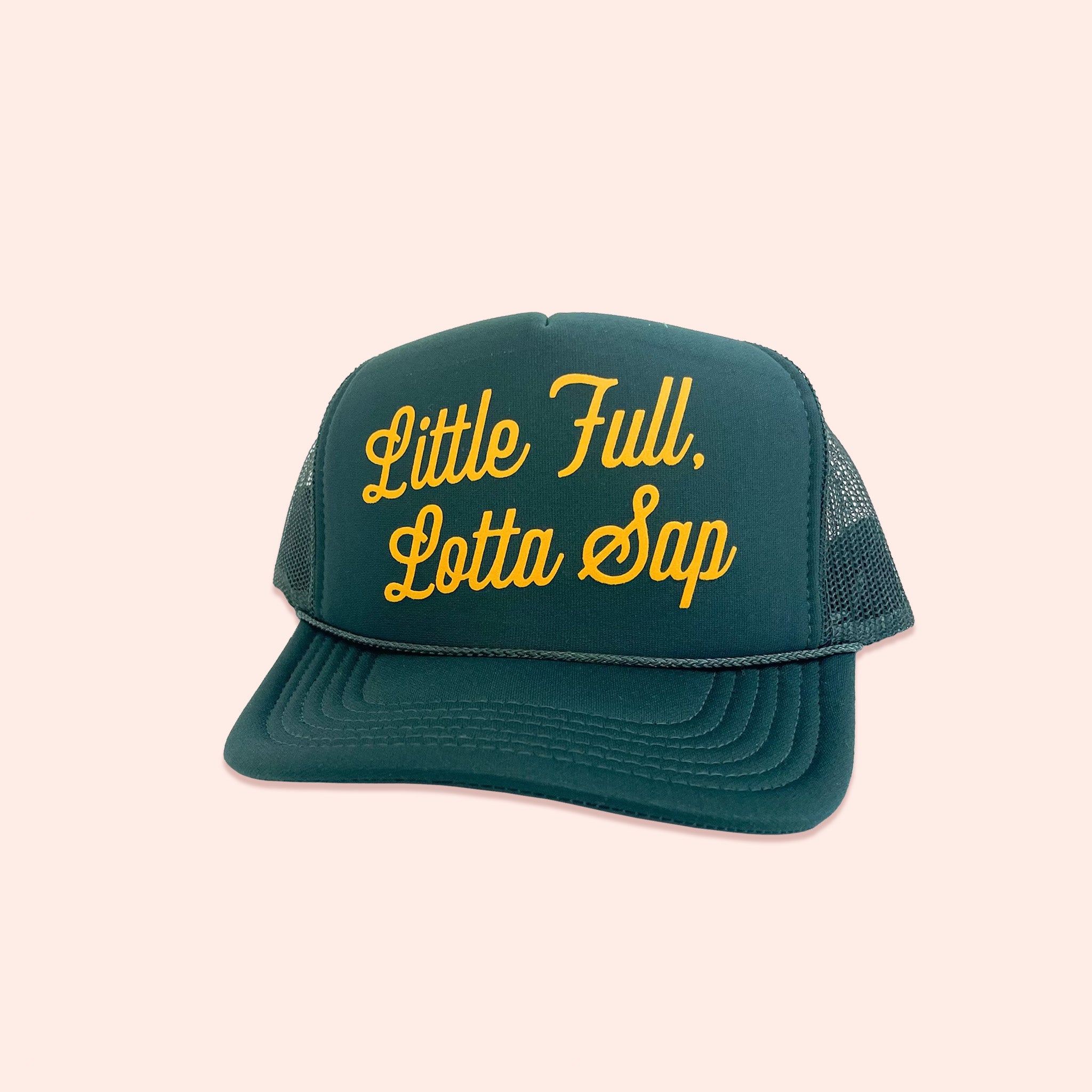 On a light pink background sits a dark green truckers hat. In sunny mustard lettering it says "Little Full, Lotta Sap."