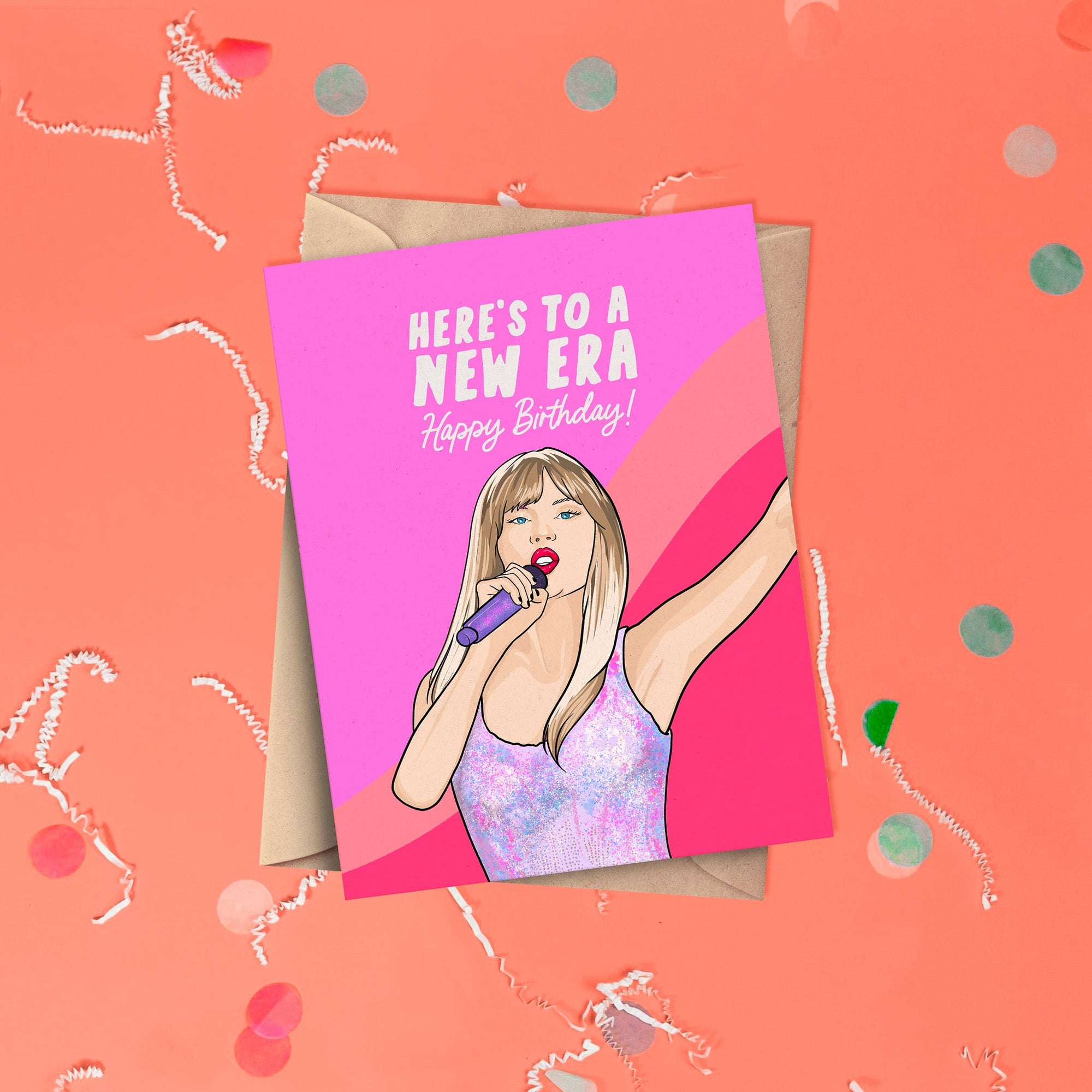 On a coral pink background sits a card with white crinkle and big, colorful confetti scattered around. This Taylor Swift inspired card has wavy colors of pink, coral, and hot pink. There is an illustration of Taylor Swift singing and it says "HERE'S TO A NEW ERA Happy Birthday!" in white lettering. It has a kraft envelope.