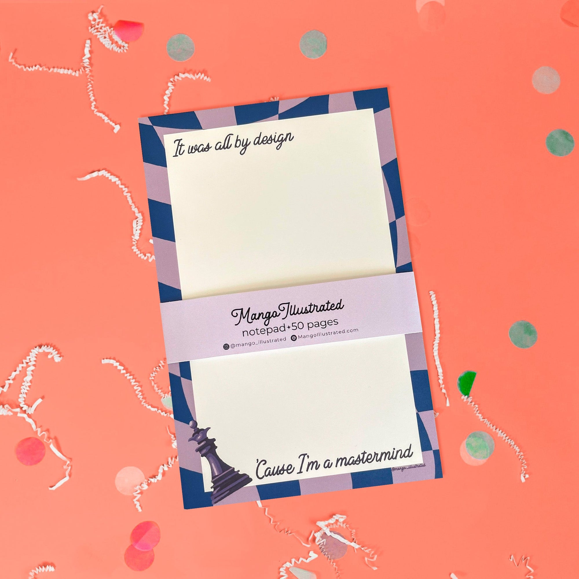 On a coral pink background sits a notepad with white crinkle and big, colorful confetti scattered around. This Taylor Swift inspired notepad is in navy and lavender with a cream background and it says at the top "It was all by design" in black script lettering and at the bottom it says "'Cause I'm a mastermind" in black script lettering. There is a chess piece illustration.