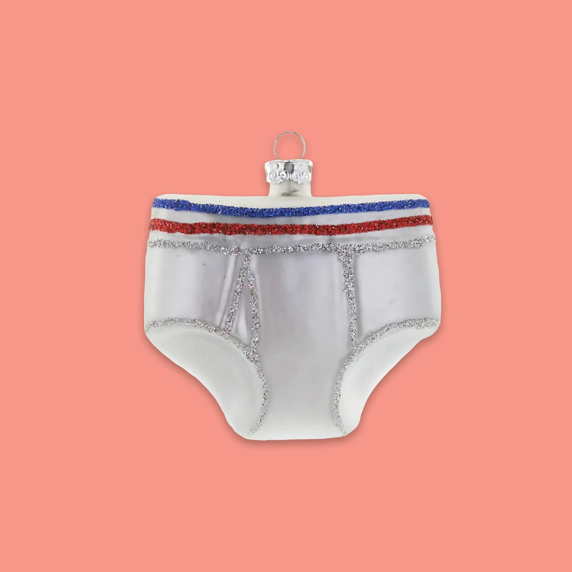 On a coral pink background sits a glass ornament of a pair of men's underwear. It is white with blue, red, and silver glitter stripes in the band.