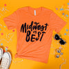 On a sunny mustard background sits a t-shirt with white crinkle and big, colorful confetti scattered around. There are mini disco balls, sunglasses, and a pair of white sneakers. This soft orange tee features custom hand lettering in navy ink and says "Midwest is BEST."