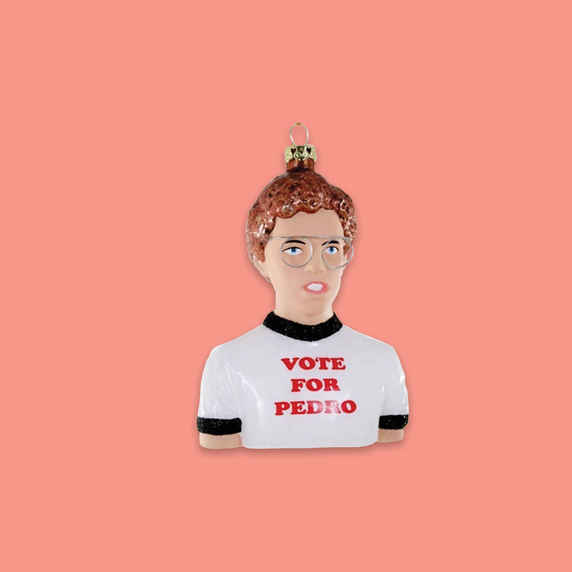 On a coral pink background sits an ornament. This Napoleon Dynament inspired glass ornament is a bust of Napoleon Dynamite himself. He is wearing the famous 'VOTE FOR PEDRO' tee.