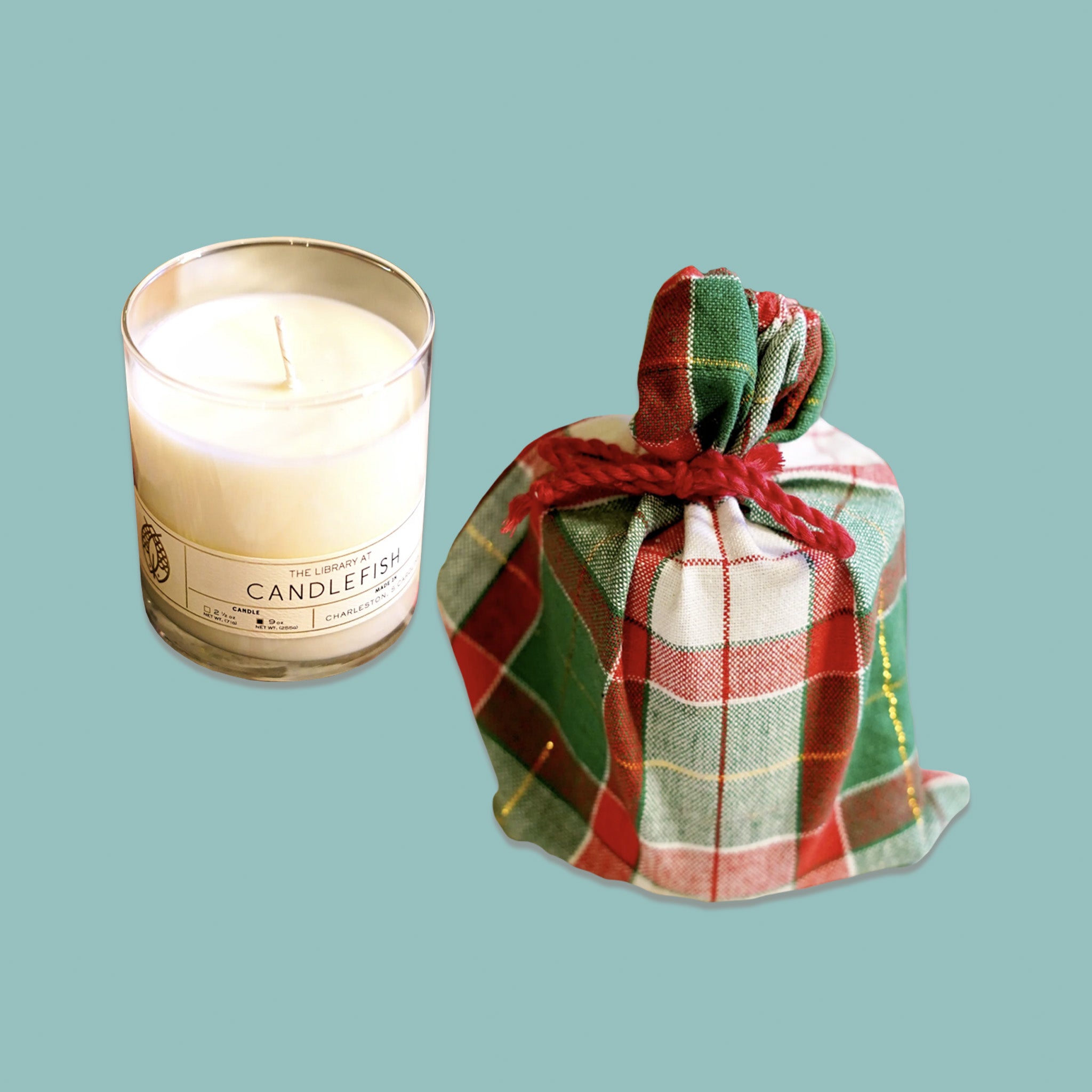 On a sage green background sits a classic library jar candle with a white plaid bag next to it. It is a '100% soy wax candle with a burn time of 15-20 hours for 2.5 ounces and 60-70 hours for 9 ounces'. 'Fragrance Notes: Nutmeg, Geranium, Frankincense. Fragrance Family - ORIENTAL'.