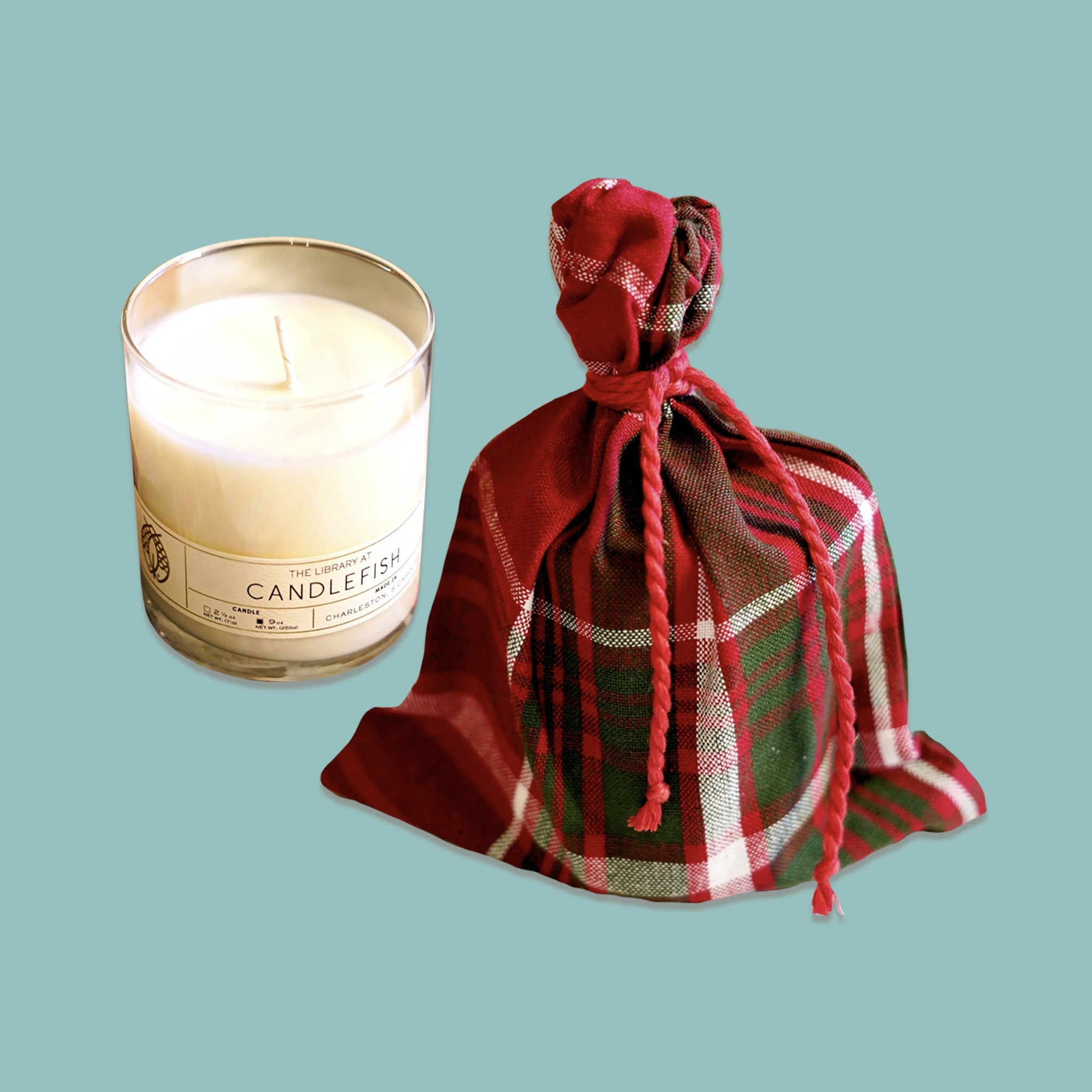 On a sage green background sits a classic library jar candle with a white plaid bag next to it. It is a '100% soy wax candle with a burn time of 15-20 hours for 2.5 ounces and 60-70 hours for 9 ounces'. 'Fragrance Notes: Nutmeg, Geranium, Frankincense. Fragrance Family - ORIENTAL'.