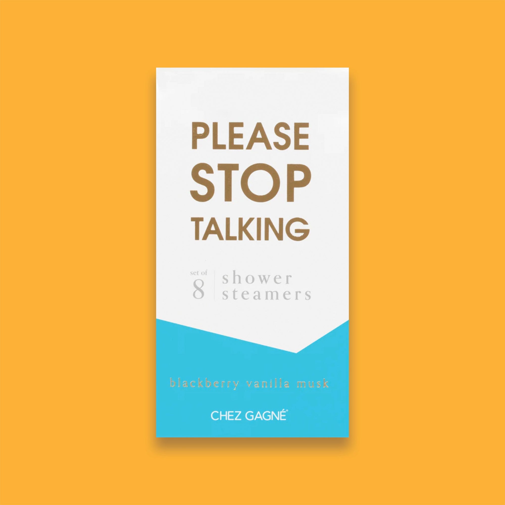 On a sunny mustard background sits a box. This picture is a close-up of a white and pacific blue package that says "PLEASE STOP TALKING" in gold foil, all caps block lettering. Under it says "set of 8" and " shower steamers" in grey, lowercase serif font. At the bottom it says "blackberry vanilla musk" in gold foil, lower case serif font.