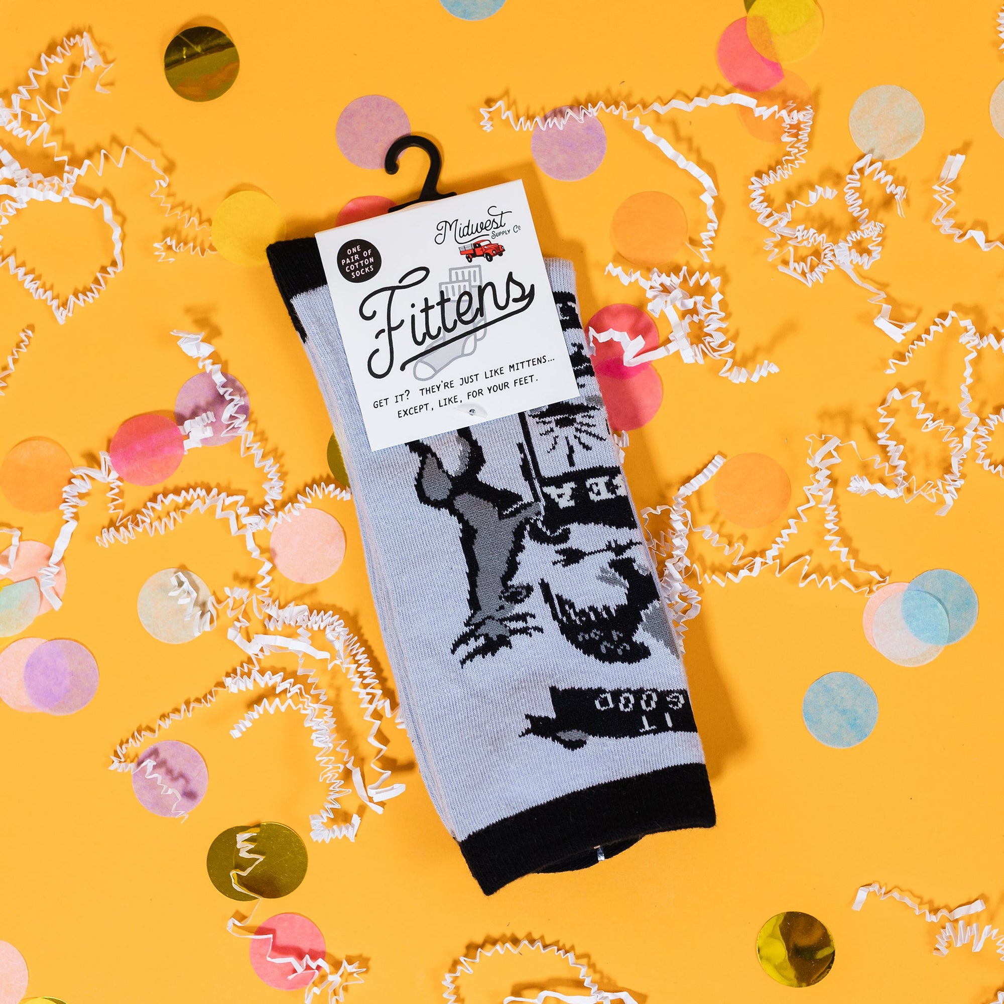 On a sunny mustard background sits a pair of socks with white crinkle and big, colorful confetti scattered around. The socks design features hand lettering and custom illustrations for a modern, lighthearted take on the flag of Michigan. It is black on grey.