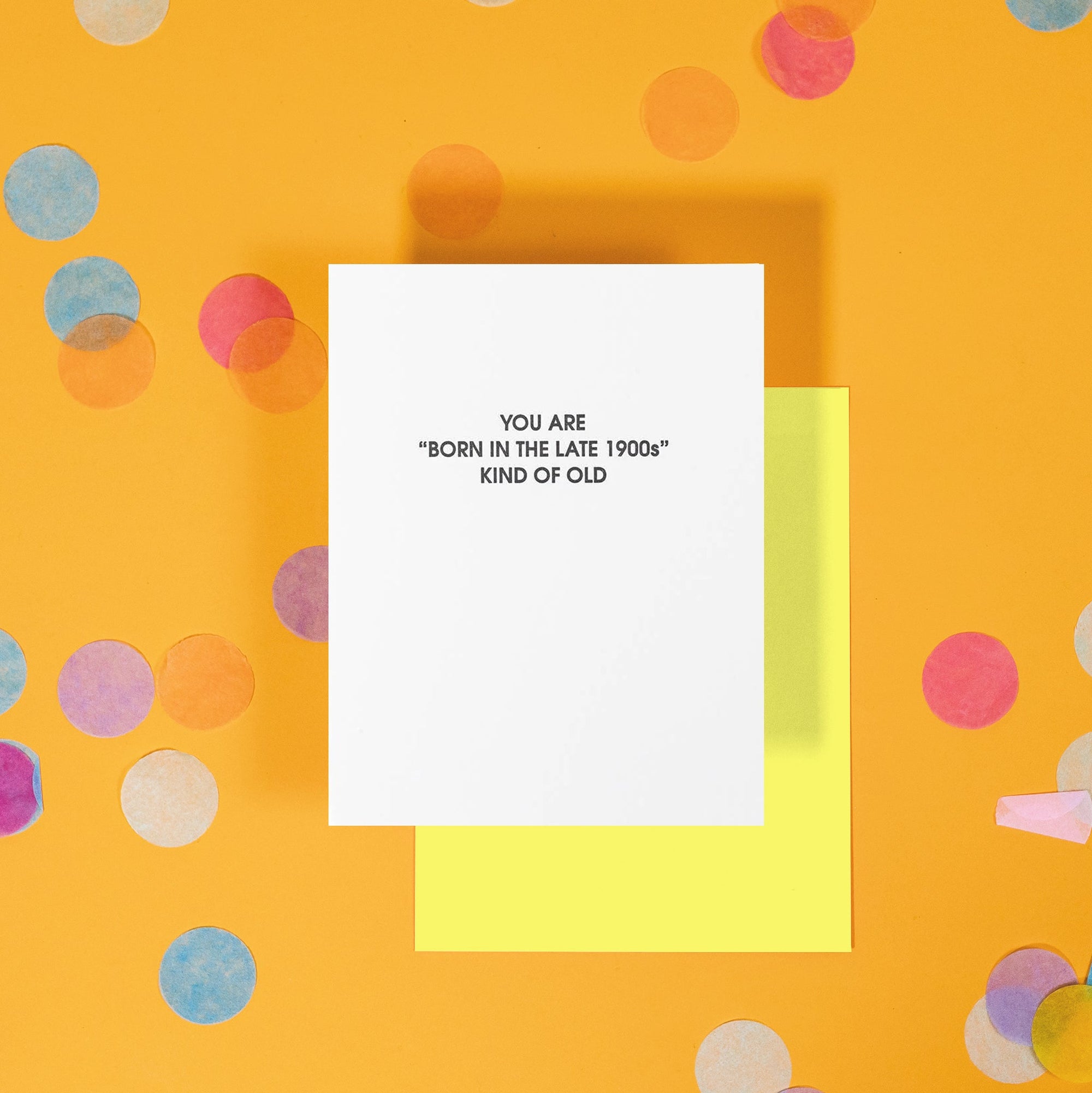 On a bright yellow background with colorful confetti sits a birthday card that reads "You are 'born in the late 1900s' kind of old."