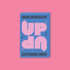 On a bubblegum pink background sits a box of UP UP Dark Chocolate. The packaging is in blue, lavender, and black. 130G 4.6 OZ