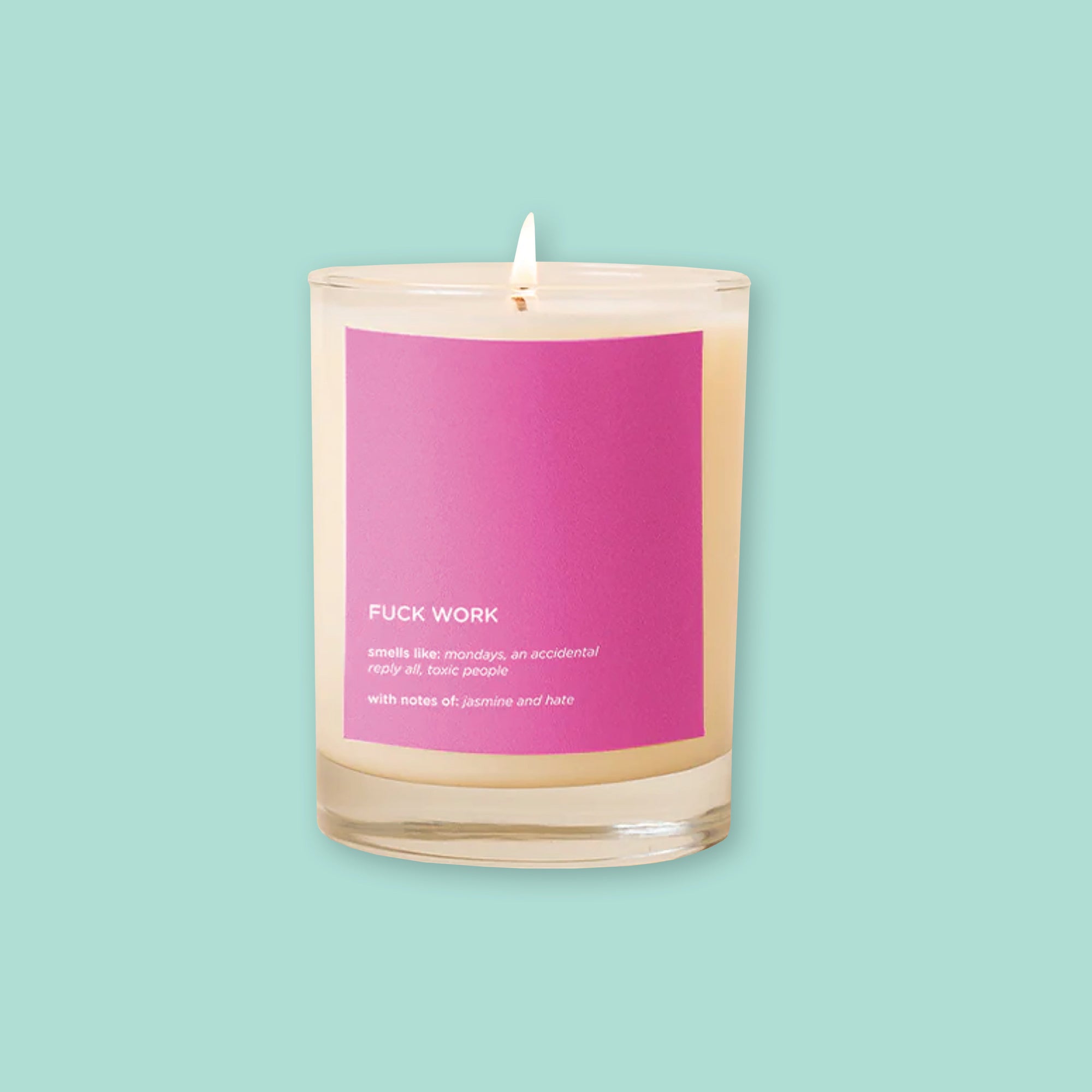 On a mint green background sits a candle. The picture is a close-up of a glass candle that is lit and has a hot pink label on the front. It says "FUCK WORK," "smells like: mondays, an accidental reply all, toxic people," "with notes of: jasmine and hate." It is in a white, block font."