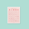 On a mint green background sits a light pink with white border bingo notepad. It is a HORRIBLE MEETING BINGO game with different work-related sayings in red lettering. Some of the sayings are "technical difficulties," "powerpoint issues," "meeting goes long," "someone arrives late," and "having a meeing to have a meeting." 