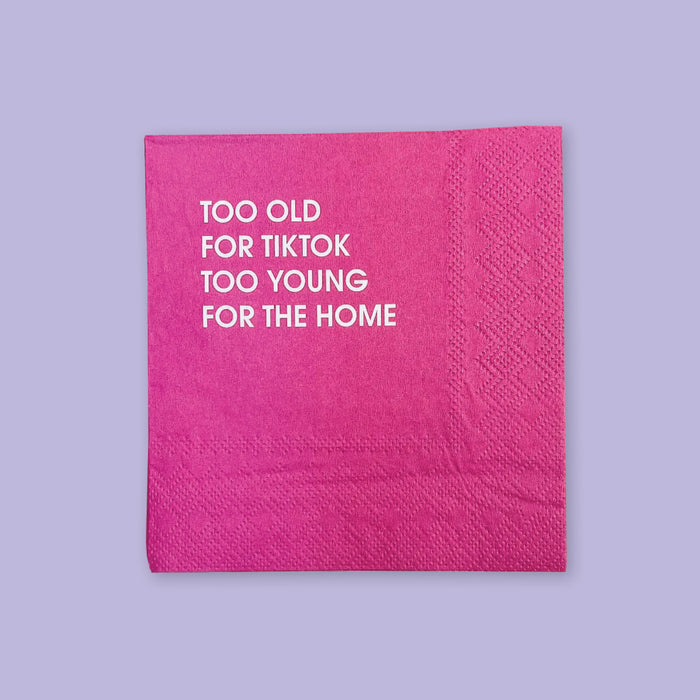 On a lavender background sits a hot pink napkin. It says "TOO OLD FOR TIKTOK TOO YOUNG FOR THE HOME" in white, all caps block font.