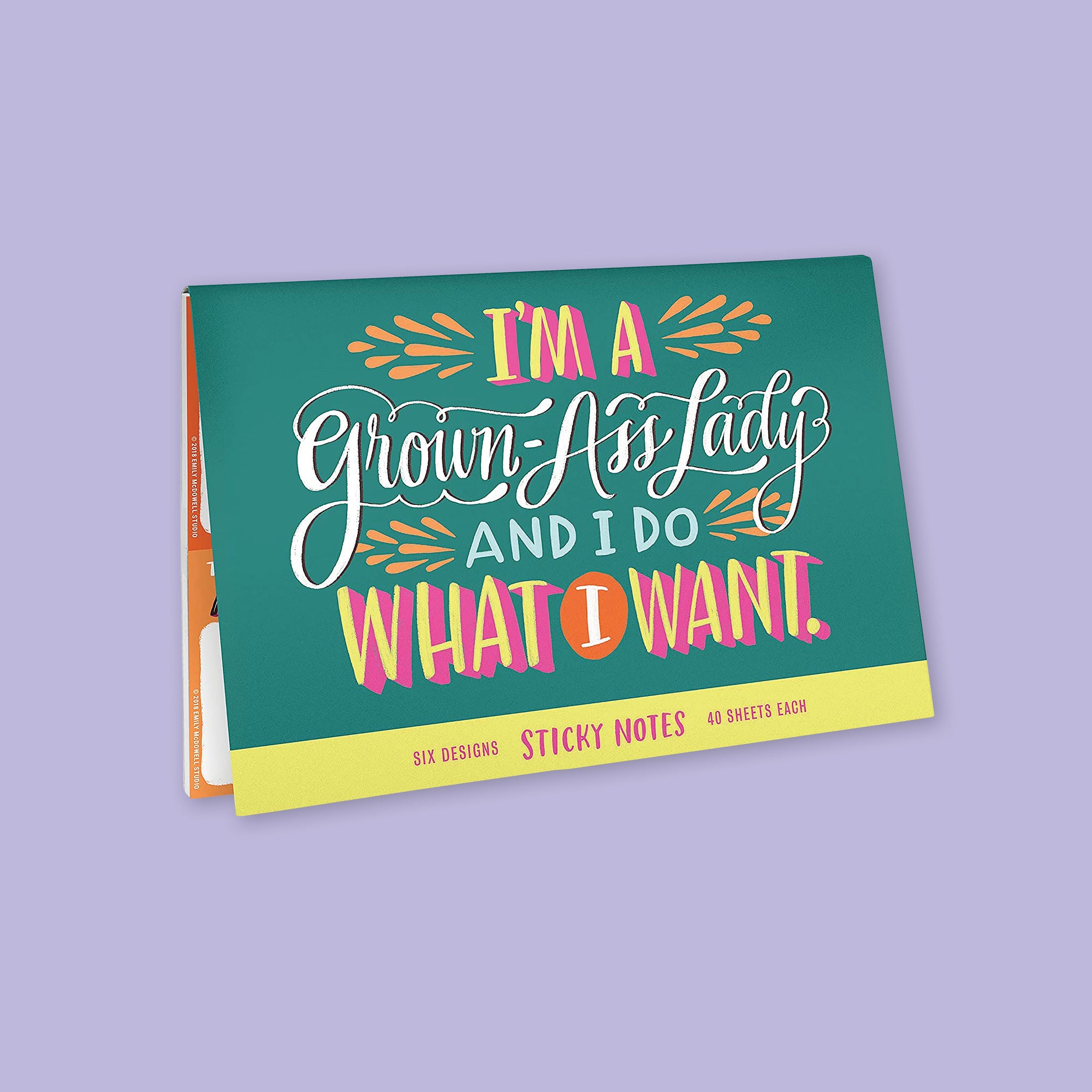 On a lavender background sits a package. The front of this sticky notes package is green with colorful writing on it. It says "I'M A Grown-Ass Lady AND I DO WHAT I WANT." in handwritten lettering. The colors are orange, yellow, hot pink, light blue, and teal. Six designs, 40 sheets each