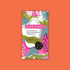 On an orangey-red background sits a package. This colorful package has different shapes in white, army green, hot pink, and light teal blue. It says "CROW & MOSS" in white, all caps block font on a hot pink background. It also says in black "COCONUT MACAROON COOKIE" in all caps block font. It says "Dairy Free COCONUT MYLK CHOCOLATE" in black script and block font. 'BEAN TO BAR SMALL BATCH 40%'. 70G (2.4OZ)