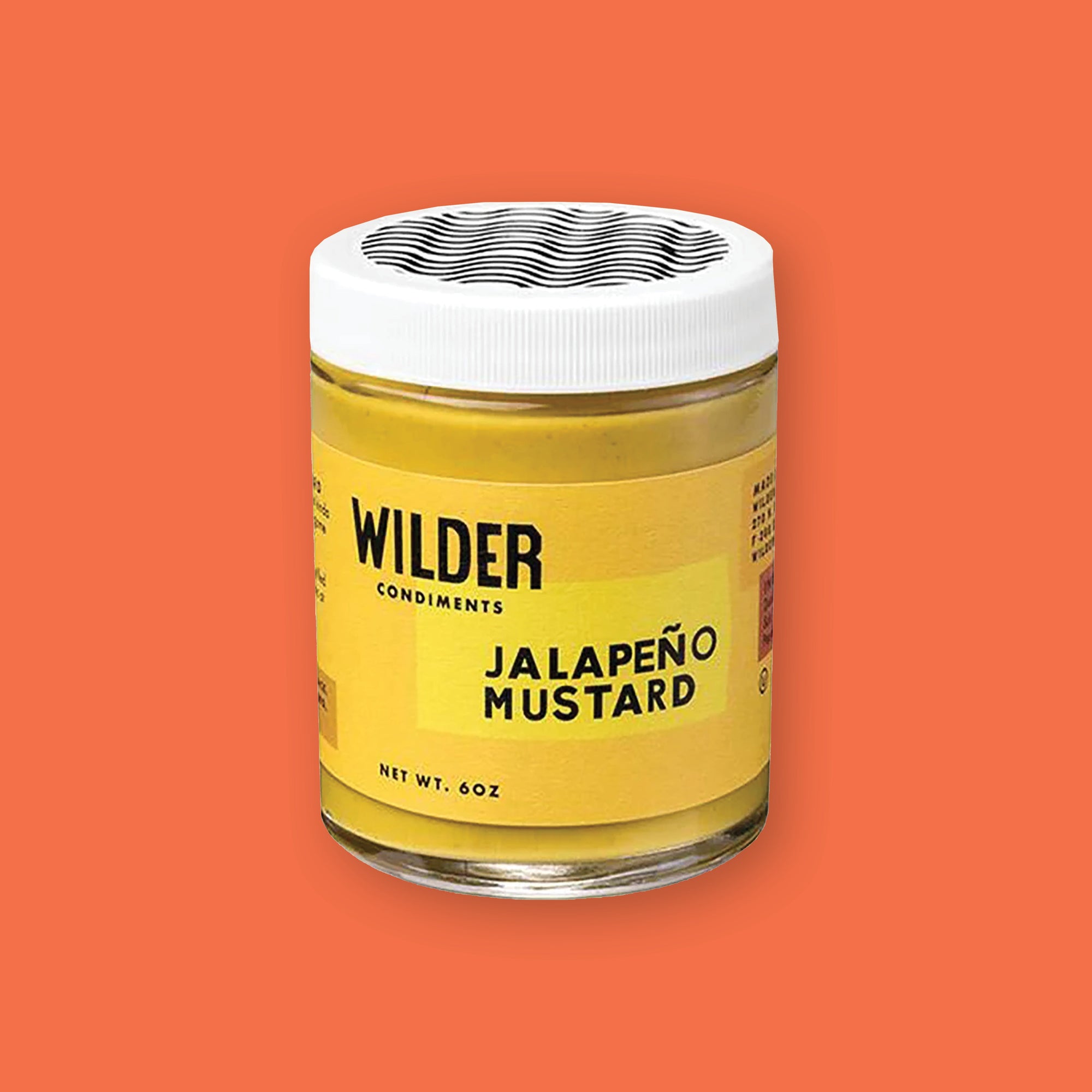 On an orangey-red background sits a jar. This jar has a white lid with black wavy lines on top and a mustard yellow label. On the label it says "WILDER CONDIMENTS" and "JALAPENO MUSTARD" in black, all caps block font. Net wt. 6oz