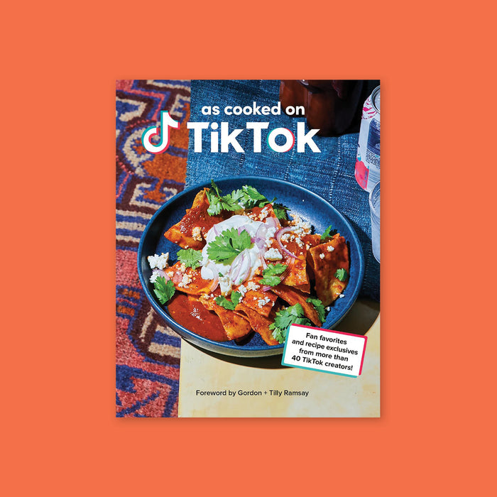 On an orangey-red background sits a book. This book has a picture of a blue bowl filled with tortilla chips, cilantro, white cheese and onions. It says "as cooked on TikTok" in a white, block font. In a white box it says "Fan favorites and recipe exclusives from more than 40 TikTok creators!" with a red and turquoise border. It also says "Foreword by Gordon + Tilly Ramsay" in black, block font.