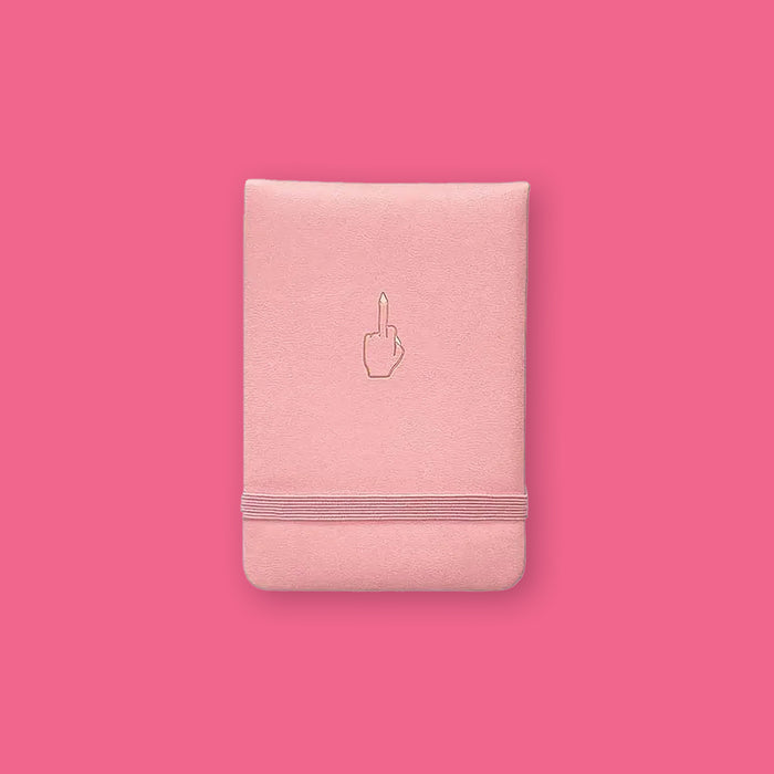 On a hot pink background sits a notebook. This light pink vegan leather, pocket journal has a middle finger in gold foil.