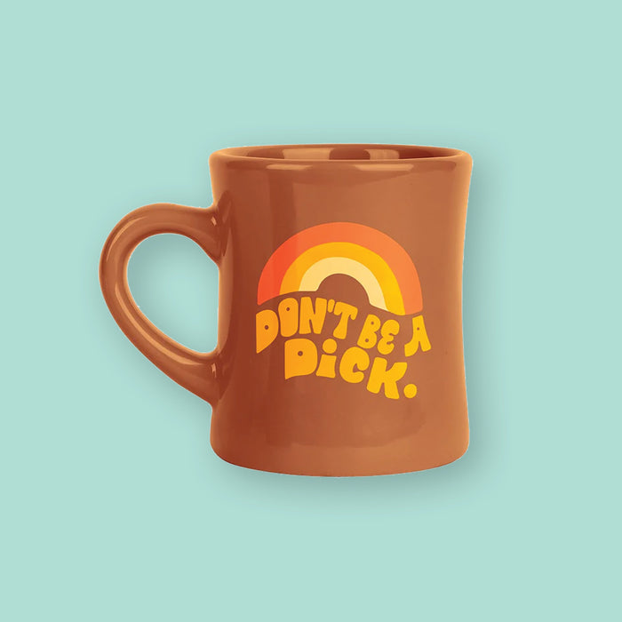 On a mint background sits a mug. The brown mug has a rainbow at the top in orange, mustard yellow, and light yellow. Under it says "DON'T BE A DiCK." in mustard yellow, thick handwritten lettering. It is a groovy design.