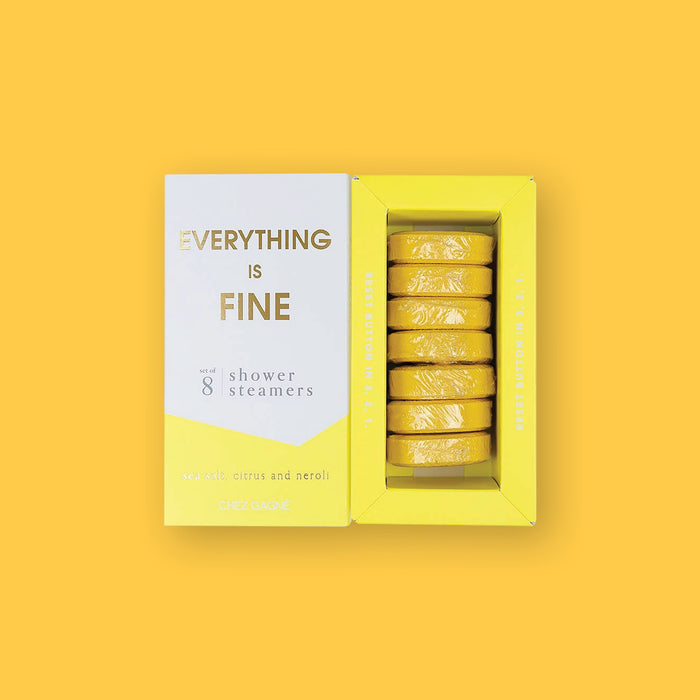 On a sunny mustard background sits two boxes. This picture is a close-up of a white and yellow package that says "EVERYTHING IS FINE" in gold foil, all caps block lettering. Under it says "set of 8" and " shower steamers" in grey, lowercase serif font. At the bottom it says "sea salt citrus and neroli" in gold foil, lower case serif font. To the right of it is a yellow box with yellow shower steamers in it.