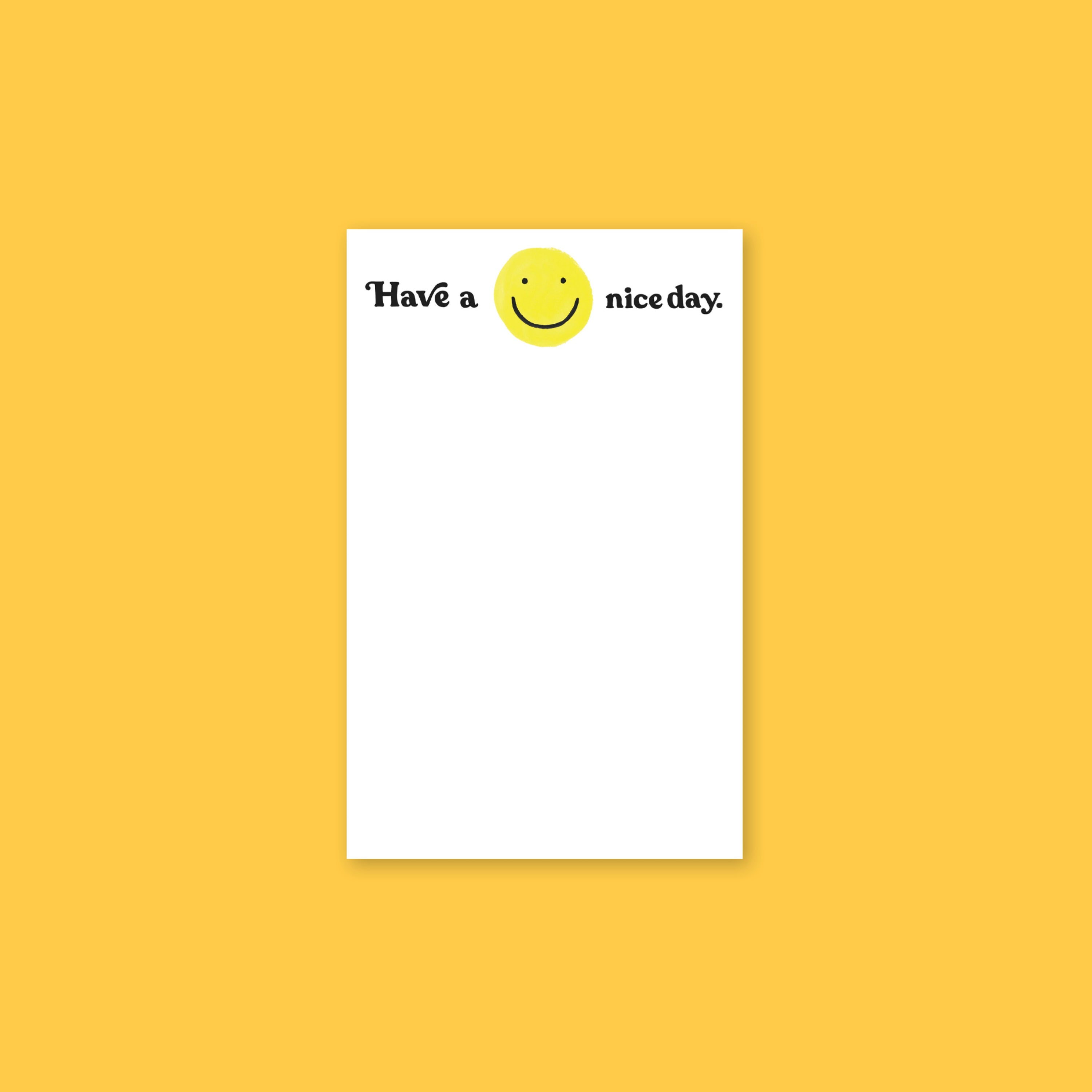 On a sunny mustard background sits a white notepad with a handdrawn yellow, smily face. It says "Have a nice day." in black, handwritten lettering.