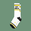 On a moss green background sits a pair of socks. These white socks have yellow and black strepes at the top and a the bottom. It says "DAY DINKER" in black, all caps block font.