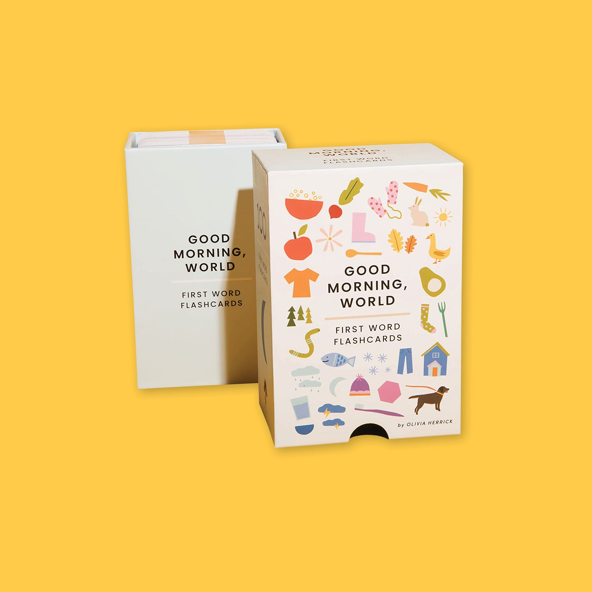 On a sunny mustard background sits a white box with a pack of 100 flash cards in a white, insert box. It says "GOOD MORNING, WORLD," and "FIRST WORD FLASHCARDS" with modern illustrations around the package. There are colorful illustrations of an apple, popcorn, radish, boots, mittens, carrot, rabbit, sun, goose, pear, socks, fork, house, pants, dog, toothbrush, hat, snow, moon, clouds with rain and lighting, glass of water, worm, trees, and a shirt. 