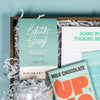 On a calming blue background sits a wooden tray of products and white paper krinkle. The products are a lovely sky blue and aqua theme. This photo is a close-up of the Edith Grey Black Tea from Big Heart Tea in its cute aqua packaging with hand-lettered text.