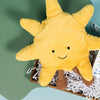 On a calming blue and green background with sunny yellow cutout sits a wooden tray of four baby themed products and white paper krinkle. This is a close-up on the yellow smiling sun Jellycat plushie.