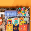 On a funky yellow and yellow-orange background sits a wooden tray filled to the brim with rainbow baby toys. This photo is a close-up of a blue bottle of Blueberry Gel tear-free bubbles, Alphatrain board book by Stephanie Miles and Christin Farley and a Manhattan Toy Atom Teether.