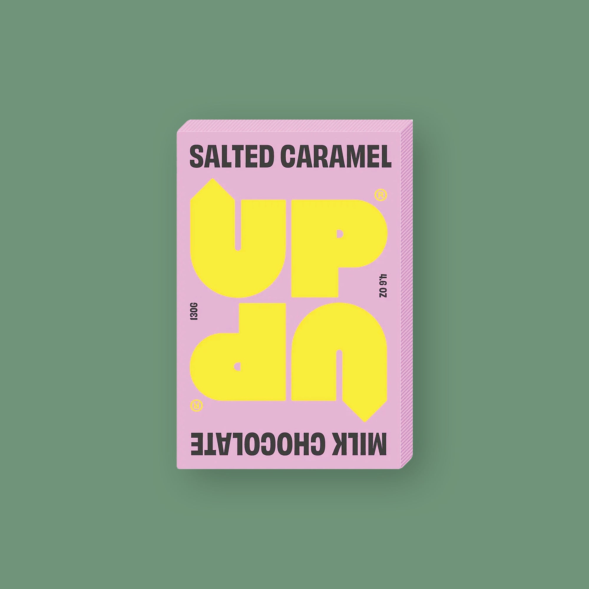 On a mossy green background sits a box of UP UP Salted Caramel Chocolate. The packaging is in light pink and yellow. 130G 4.6 OZ