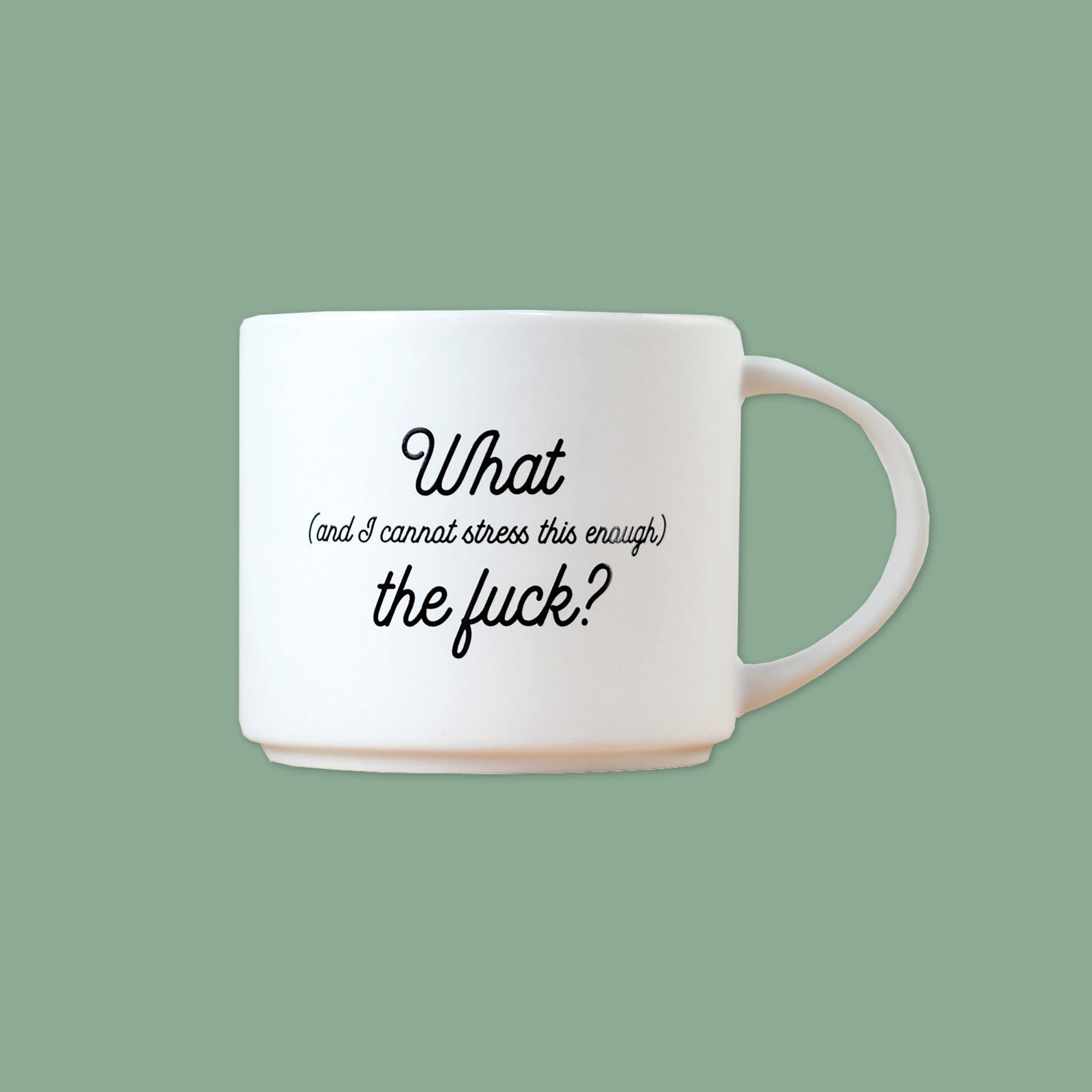 On a moss green background sits a mug. This white mug says "What (and I cannot stress this enough) the fuck?" in black script font.