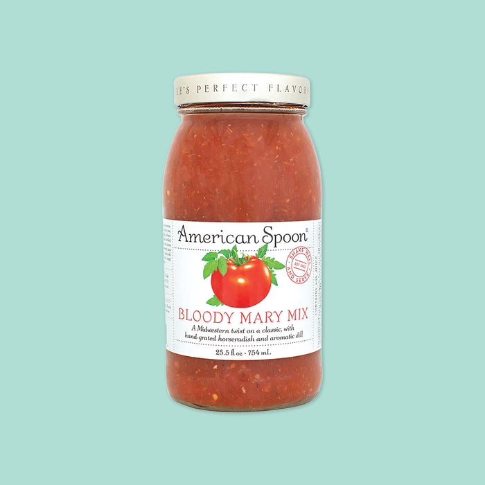 On a mint green background sits a jar. The clear jar has a white lid and label with an illustration of a tomato with leaves. It says "American Spoon" in black, serif font. Under the tomato it says "BLOODY MARY MIX" in red, all caps serif font. It also says "A Midwestern twist on a classic, with hand-grated horseradish and aromatic dill." in black, serif font. 25.5 fl oz • 754 mL