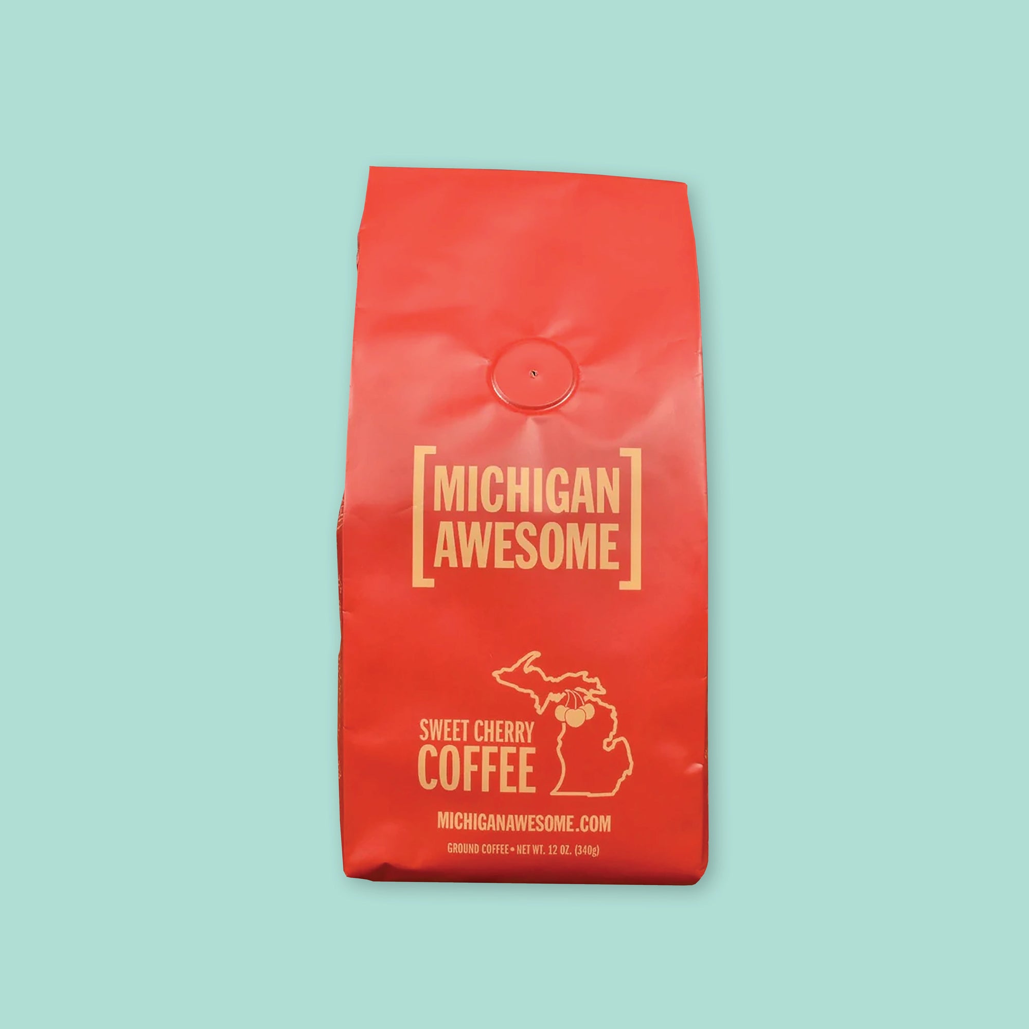On a mint green background is a red bag of coffee. The coffee is Michigan Awesome brand Sweet Cherry Ground Coffee. 12 oz (350 g)