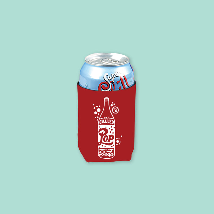 On a mint green background sits a koozie. The red koozie has a white handdrawn illustration of a pop with handdrawn lettering that says "It's Called Pop Not Soda." There is a can inside the koozie.