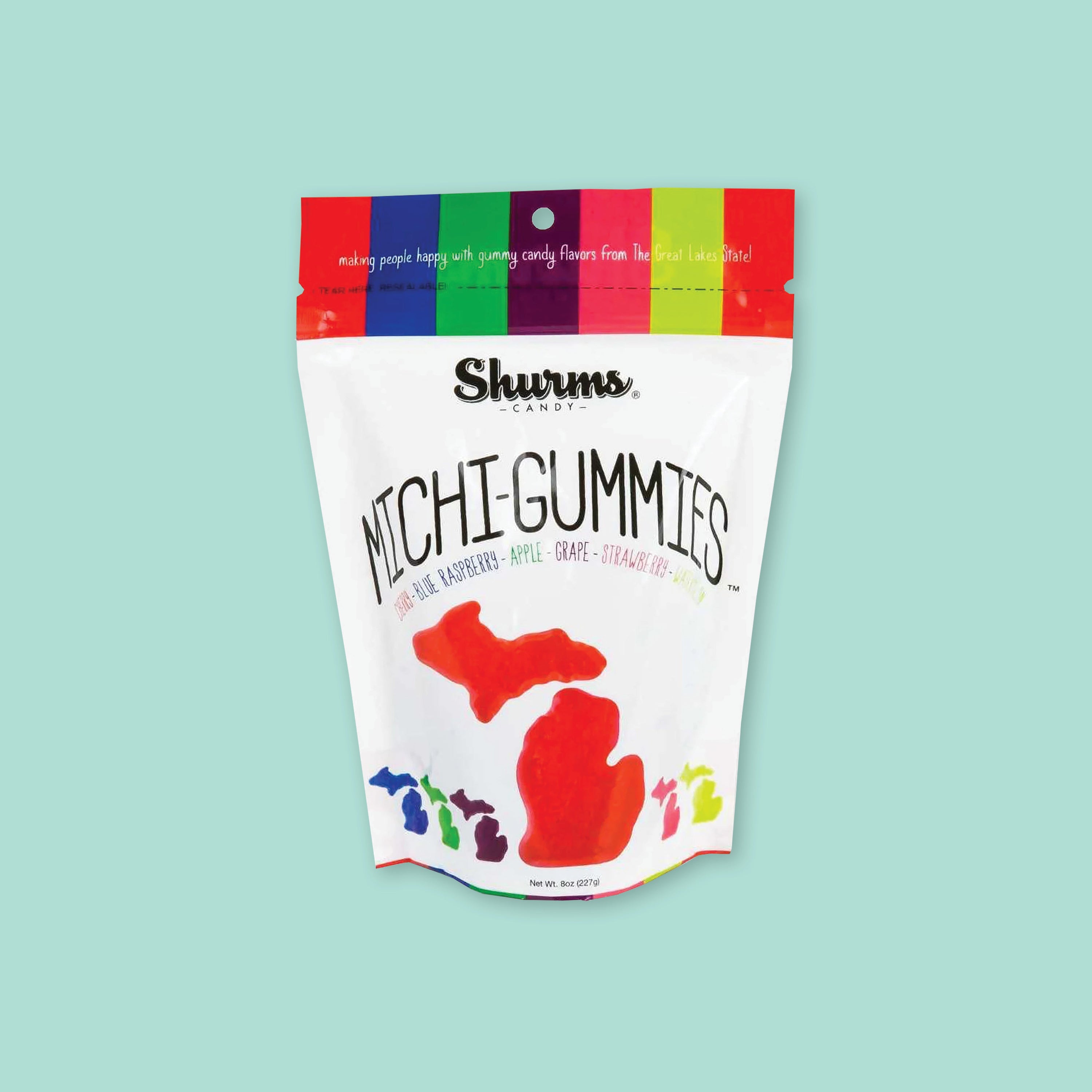 On a mint green background sits a white package. This package has colorful vertical stripes at the top in red, blue, kelly green, marroon, hot pink, chartreuse, and orangey-red. It says "making people happy with hummy candy flavors from The Great Lakes State!" in white, handwritten lettering. It also says "MICHI-GUMMIES," "CHERRY • BLUE RASPBERRY • APPLE • STRAWBERRY • WATERMELON" in all caps, various colors font. It has illustrations of colored gummies in the the shape of Michigan state. Net Wt. 8oz (227g)