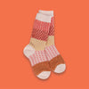 On an orange background sits the world's softest socks with different patterns in modern fall colors, including orangey-red, rust, peach, and mustard. 