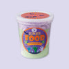 On a lavender background sits a small clear opaque deli tub of green and purple cotton candy with a Halloween label that says "Zombie Food Cotton Candy"