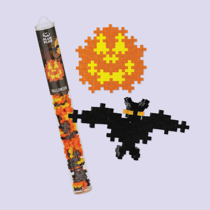 On a lavender background sits a tube of Plus Plus Halloween blocks and two possible things to make with them -- and orange pumpkin and a black bat.