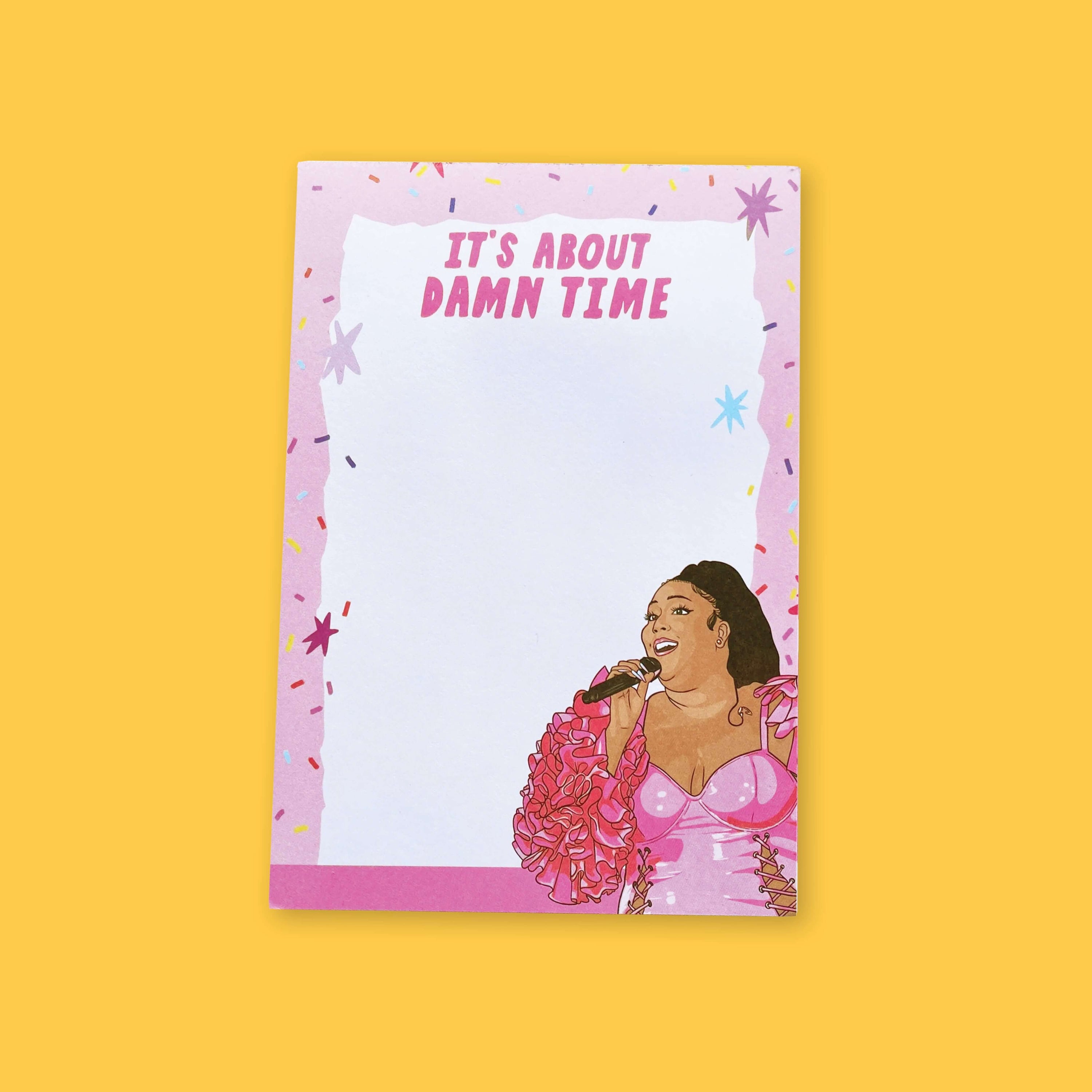 On a sunny mustard background sits a notepad. This Lizzo inspired notepard is colorful with different shades of pinks. There is a light pink border with colorful confetti and stars and a white, handdrawn box on top. At the top it says "IT'S ABOUT DAMN TIME" in hot pink, handwritten lettering. At the bottom right corner is an illustration of Lizzo with a hot pink outfit on and a microphone in her hand.