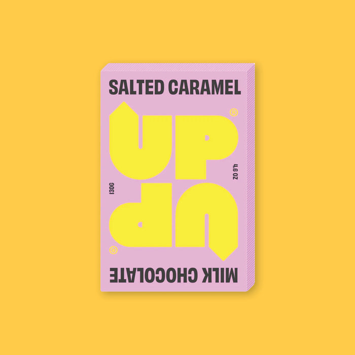 On a sunny mustard background sits a box of UP UP Salted Caramel Chocolate. The packaging is in light pink and yellow. 130G 4.6 OZ