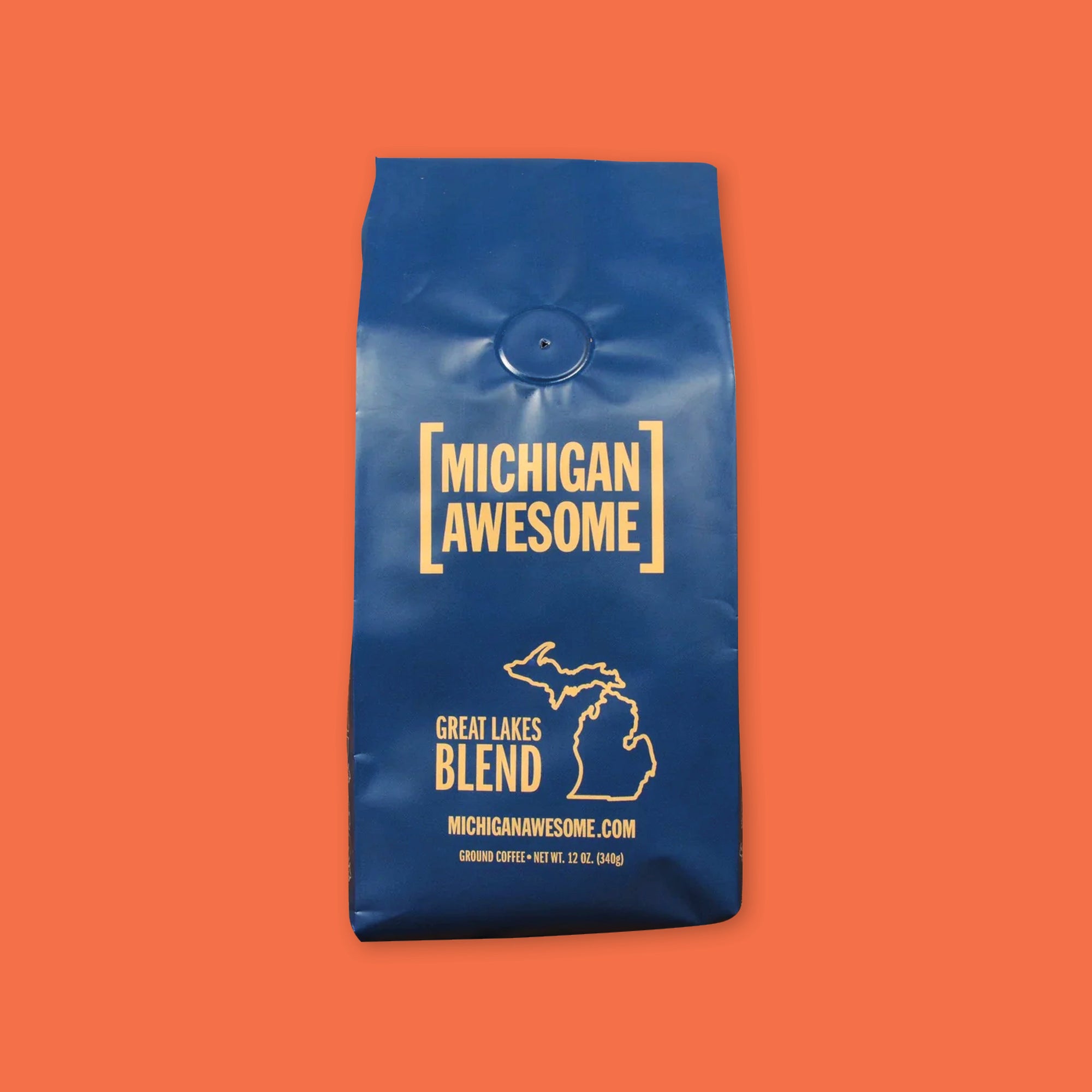 On an orangey-red backdrop is a navy blue bag of coffee is Michigan Awesome brand Great Lakes Blend. Ground coffee. 12 oz (350 g)