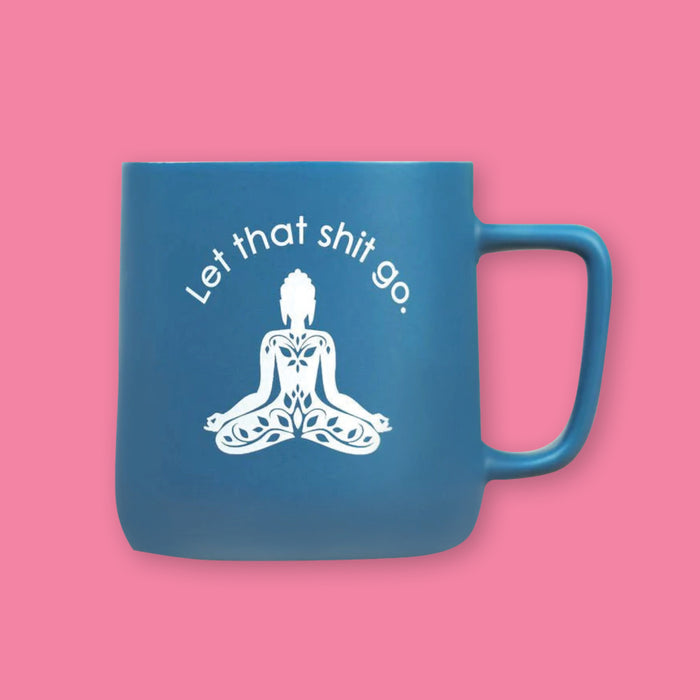 On a bubblegum pink background is a blue mug with white on the inside and on the brim. There is a buddha meditation pose in white, with white block lettering that says "Let that shit go."